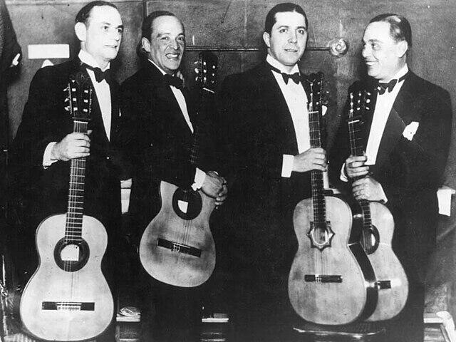 Fotografía en blanco y negro de cuatro hombres con traje y guitarra.