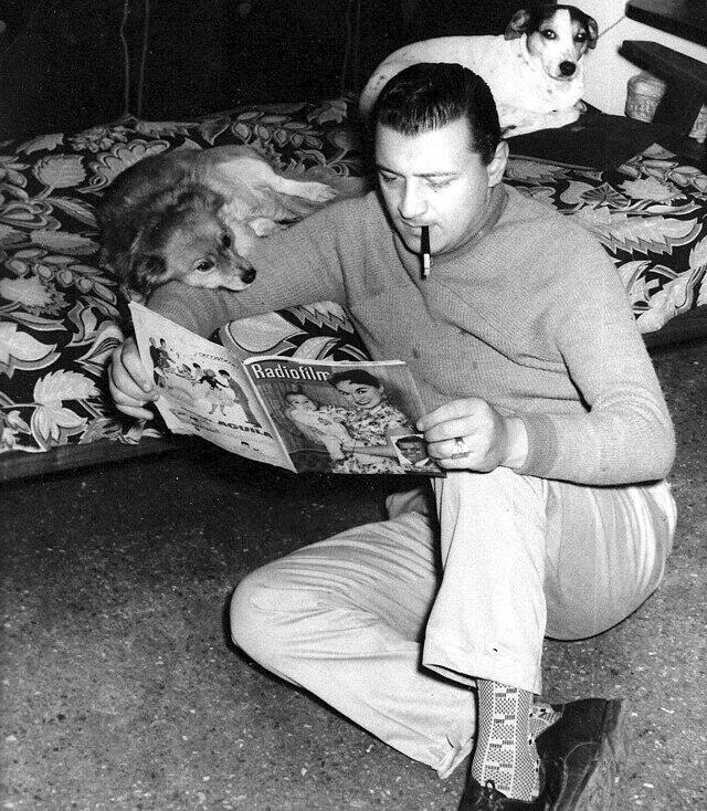 Hombre leyendo una revista junto con perros.