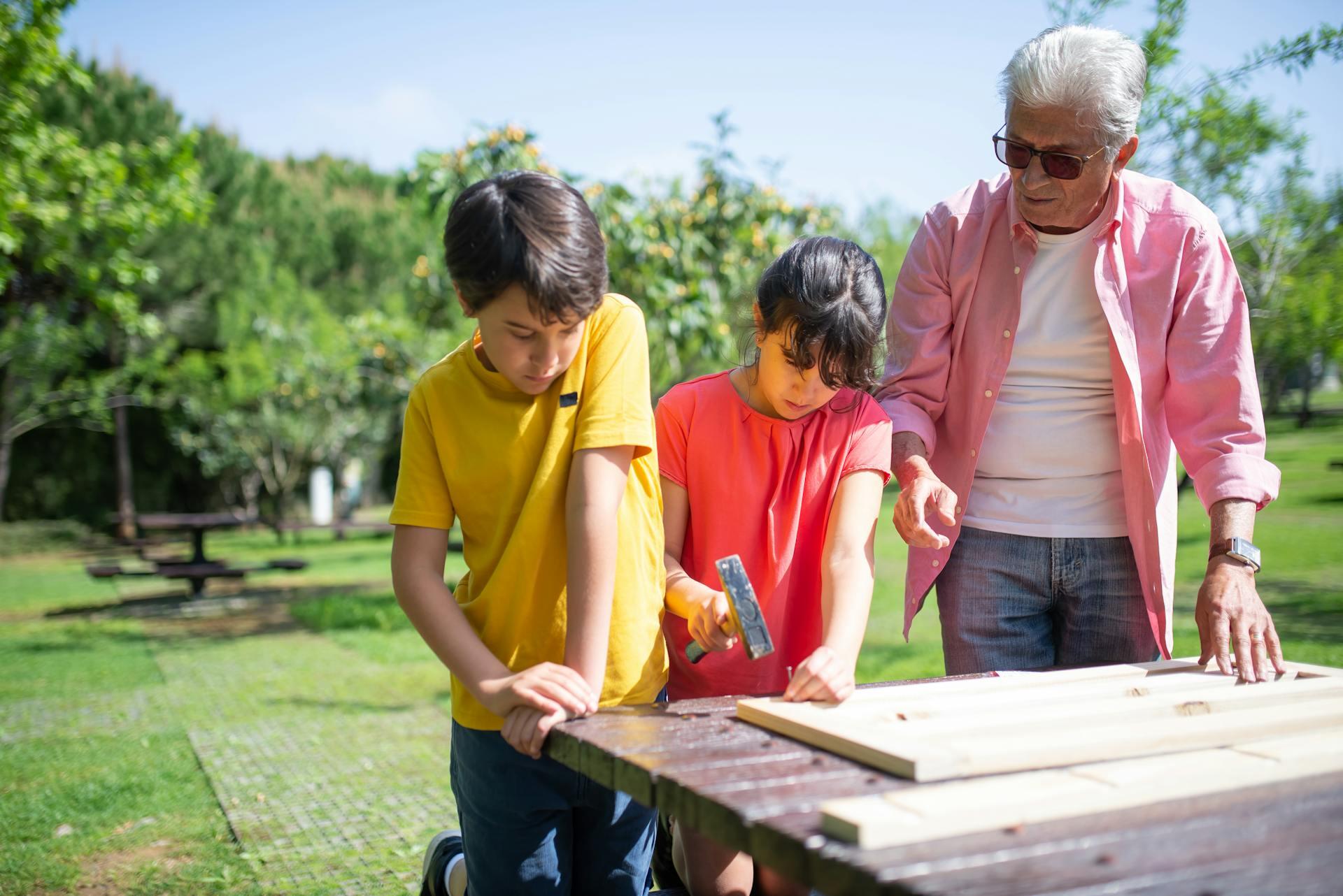 Un adulto y dos niños martillando la madera.