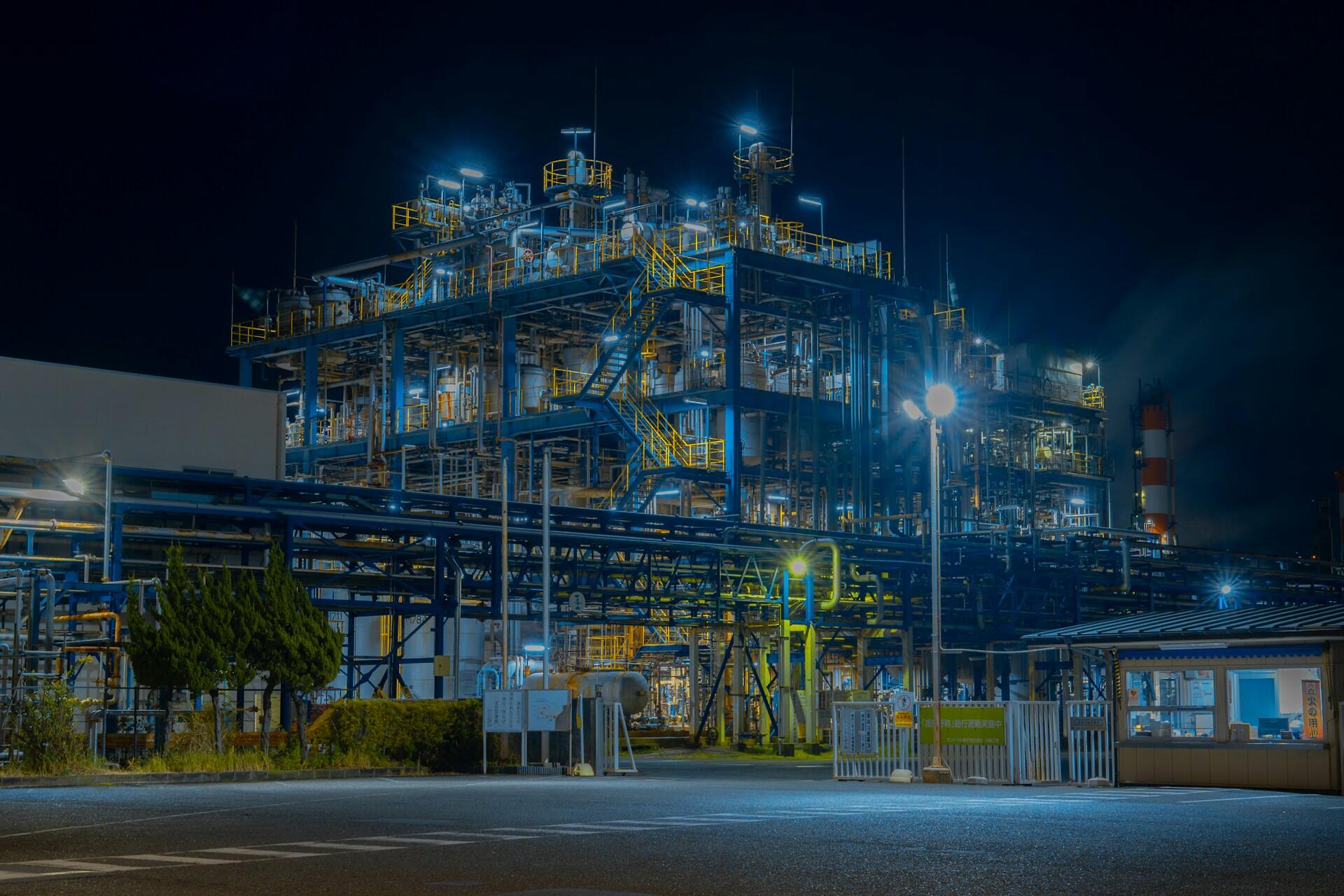 Planta industrial iluminada de noche, simbolizando la compleja infraestructura requerida para la producción a gran escala de hidrógeno. Foto de mos design en Pexels.
