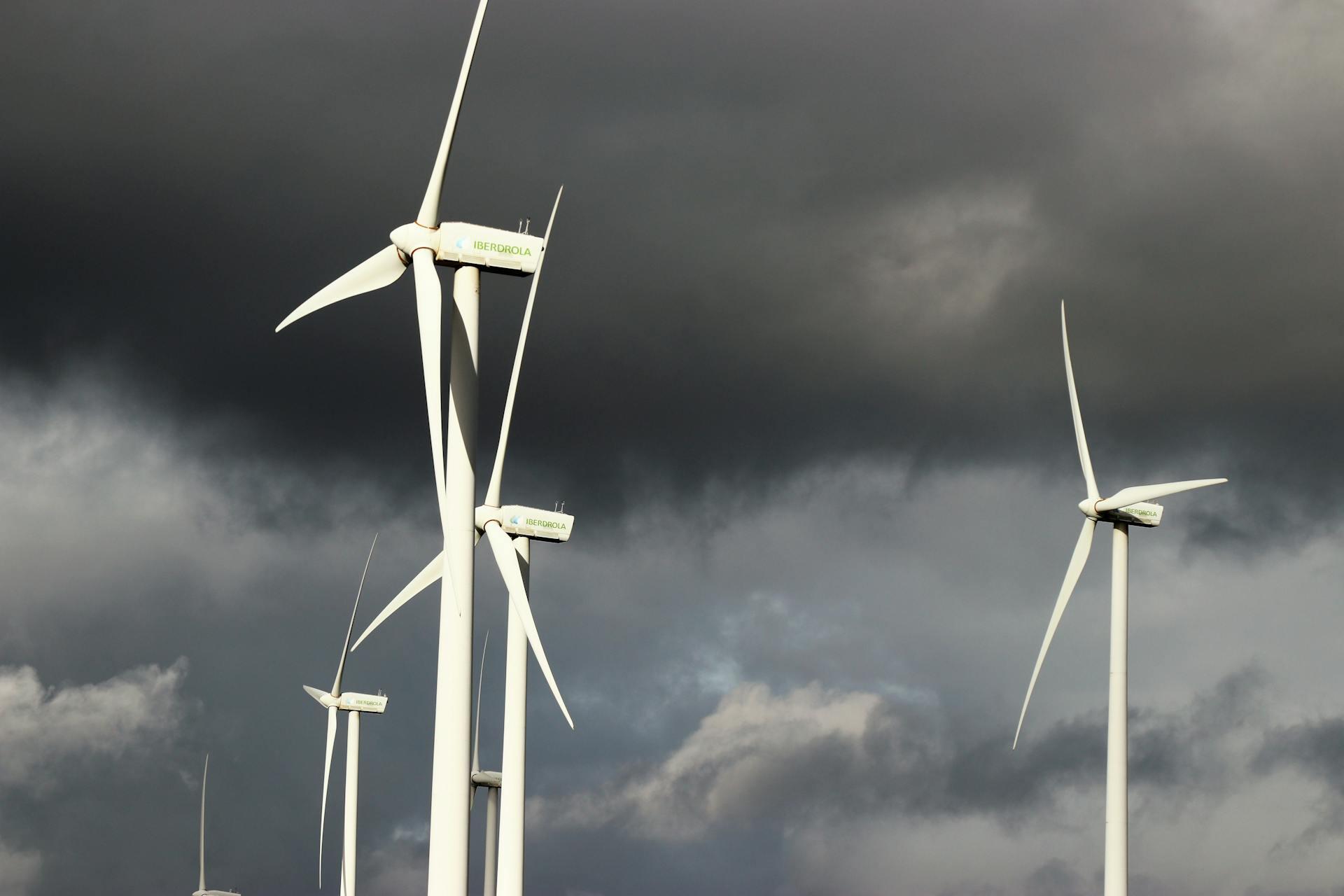 Turbinas eólicas blancas de la empresa Siemens Gamesa contra un cielo nublado y oscuro, representando la energía eólica para producir hidrógeno verde. Fotografía de Expect Best.