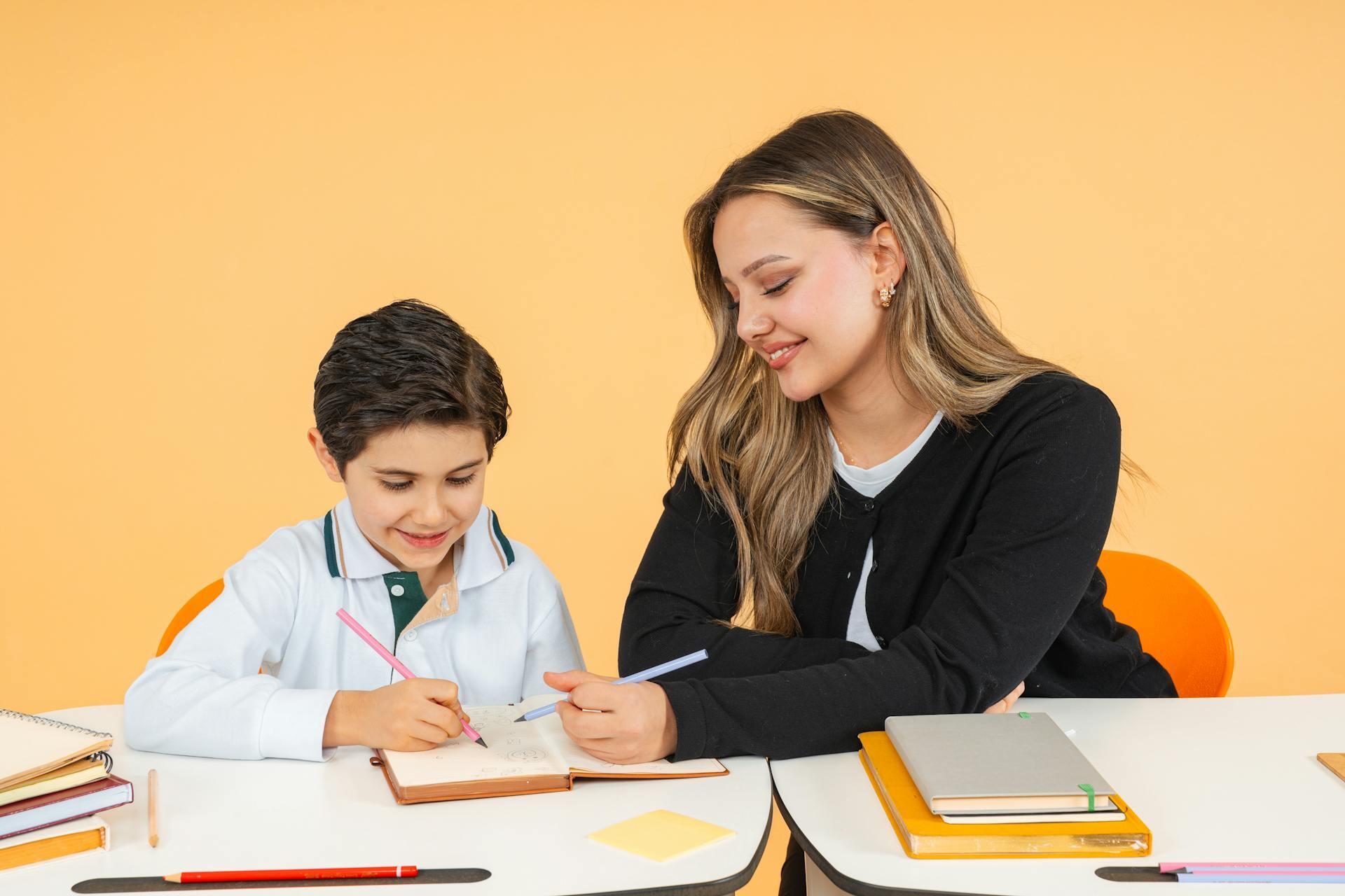 Niño y maestra sentados en la mesa con libros.