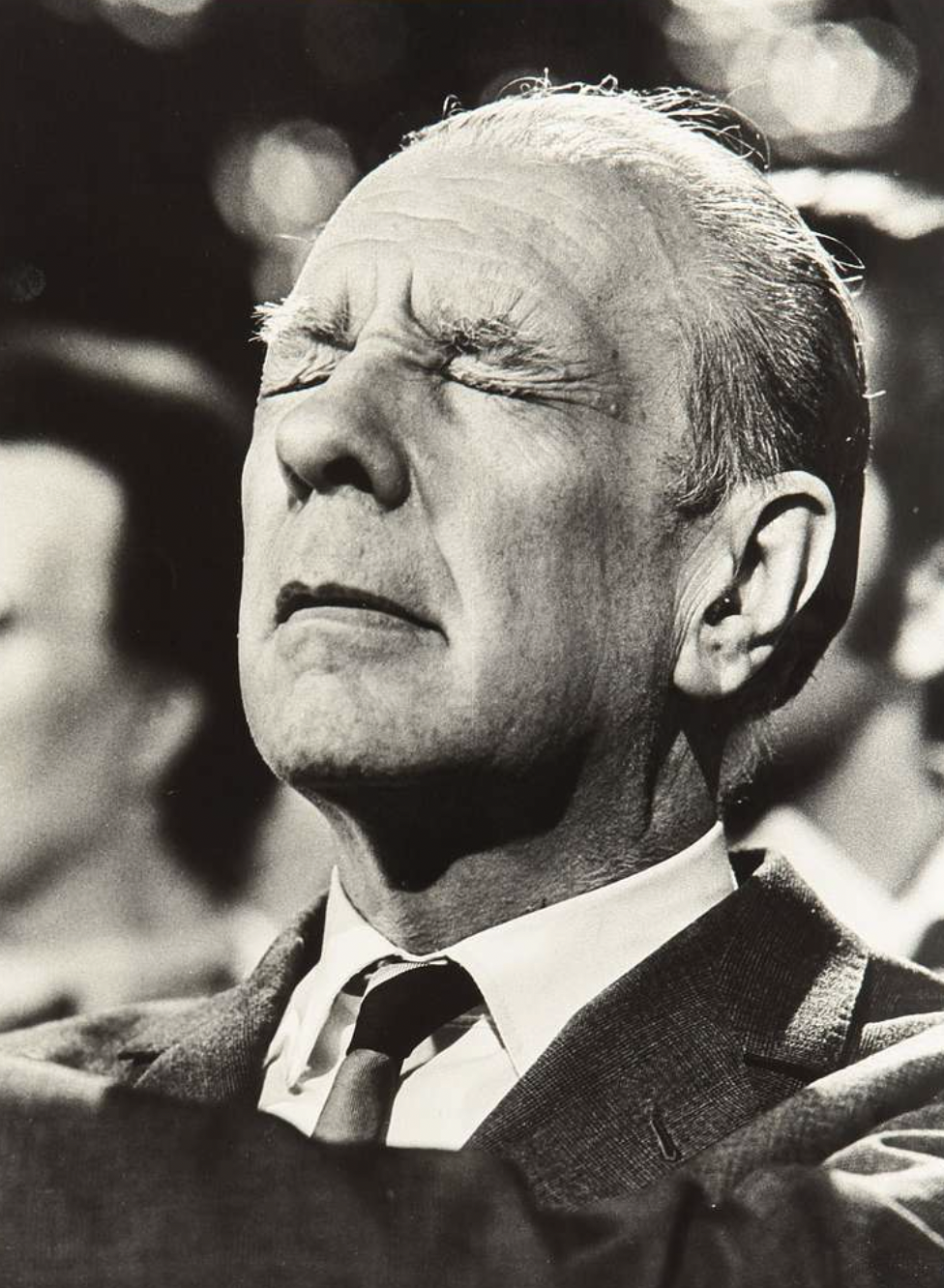 Retrato en primer plano de Jorge Luis Borges con los ojos cerrados y el rostro elevado, fotografía en blanco y negro. Fuente: Google Common License.