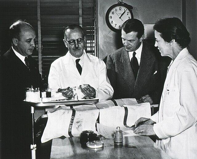 Tres hombres y una mujer parados delante del reloj de agujas.