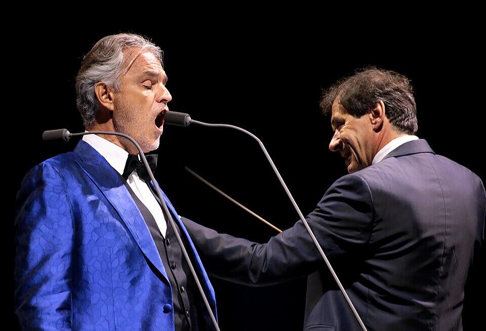 Hombre con saco azul cantando frente al micrófono.