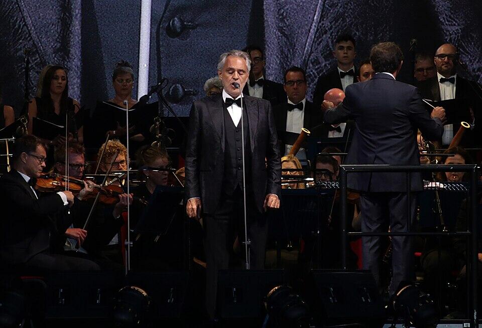 Hombre parado detrás del micrófono delante de la orquesta.