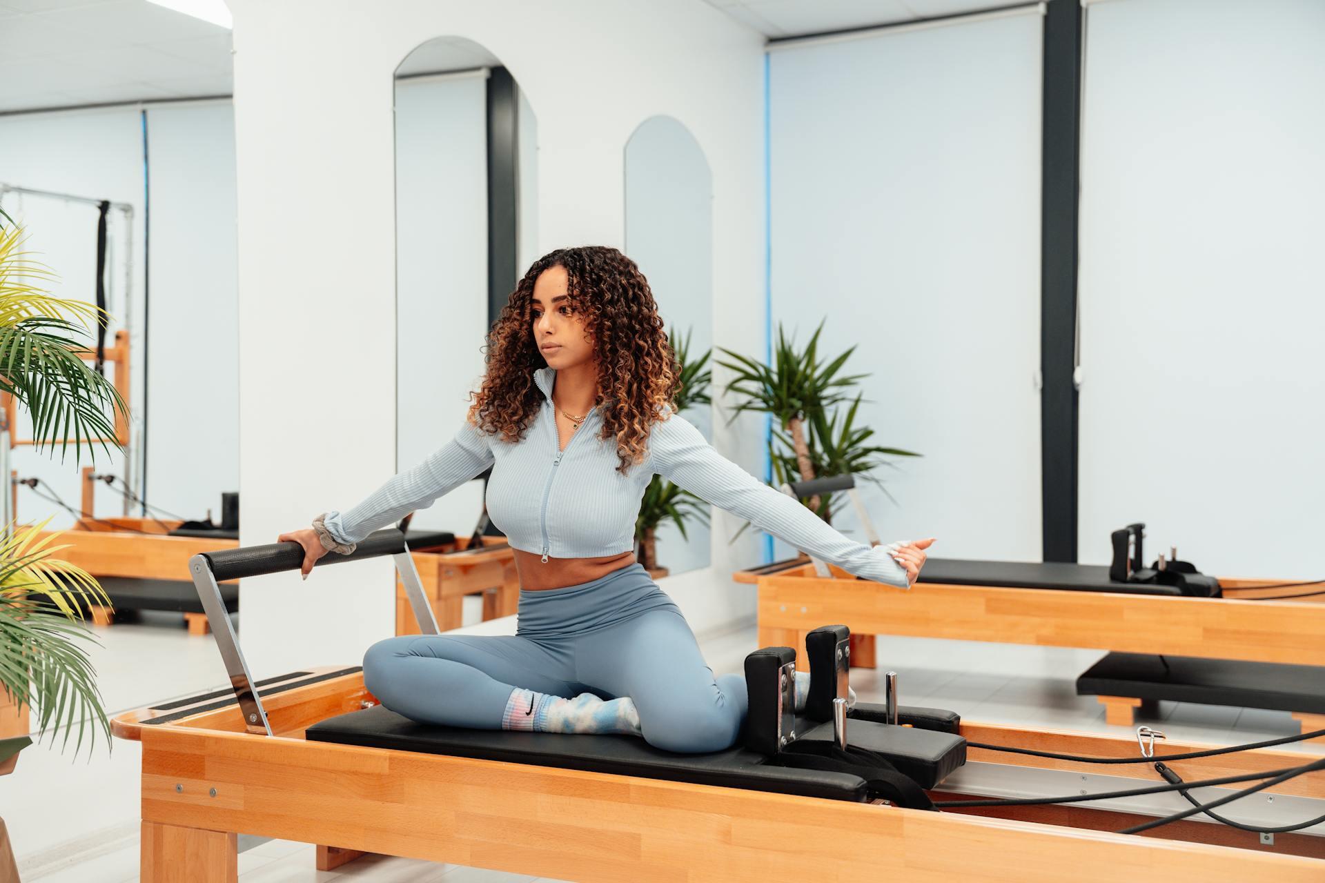 Mujer co ropa celeste sentada en la camilla de pilates.