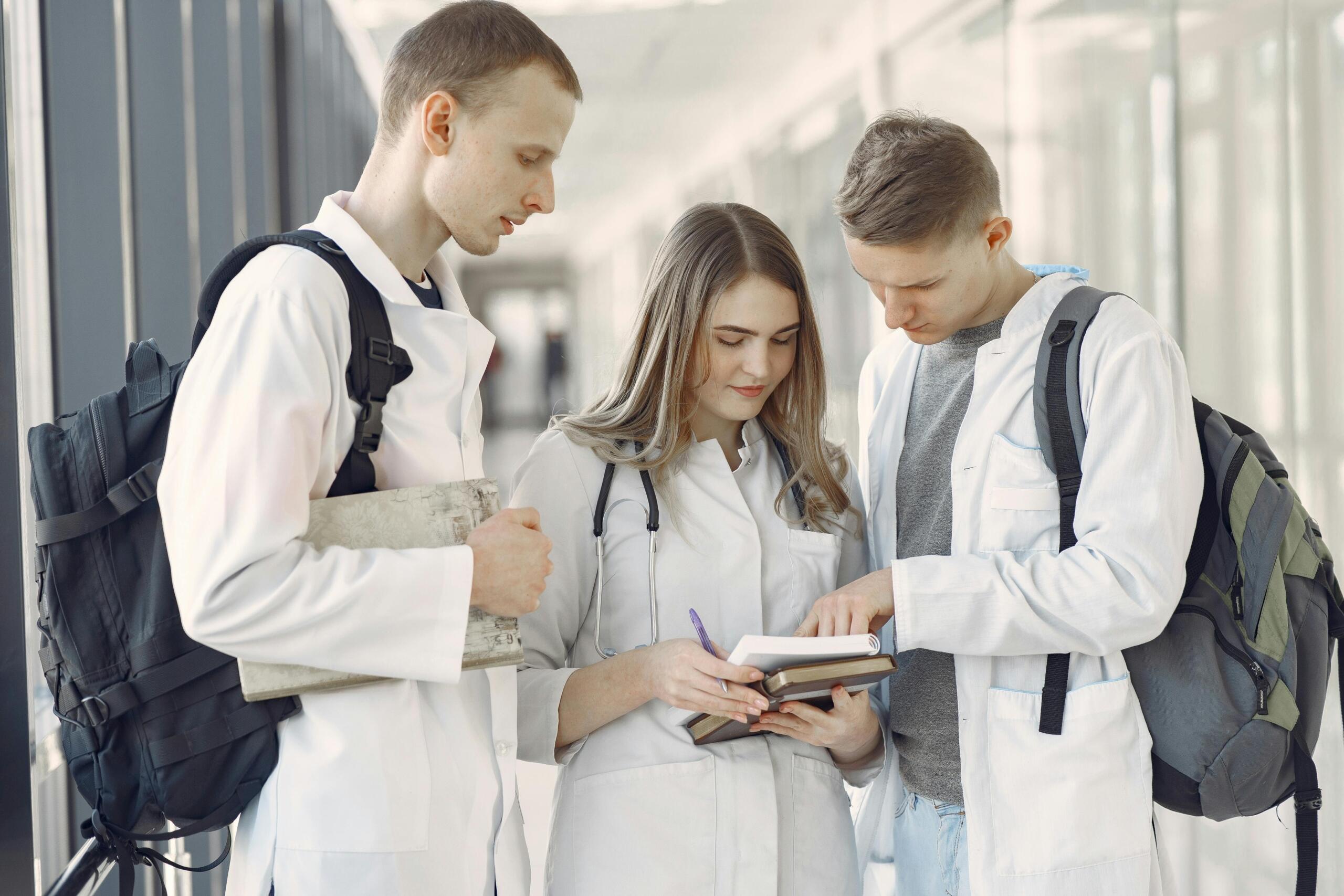 Tres estudiantes de medicina con deleantal blanco leyendo apuntes de la libreta.