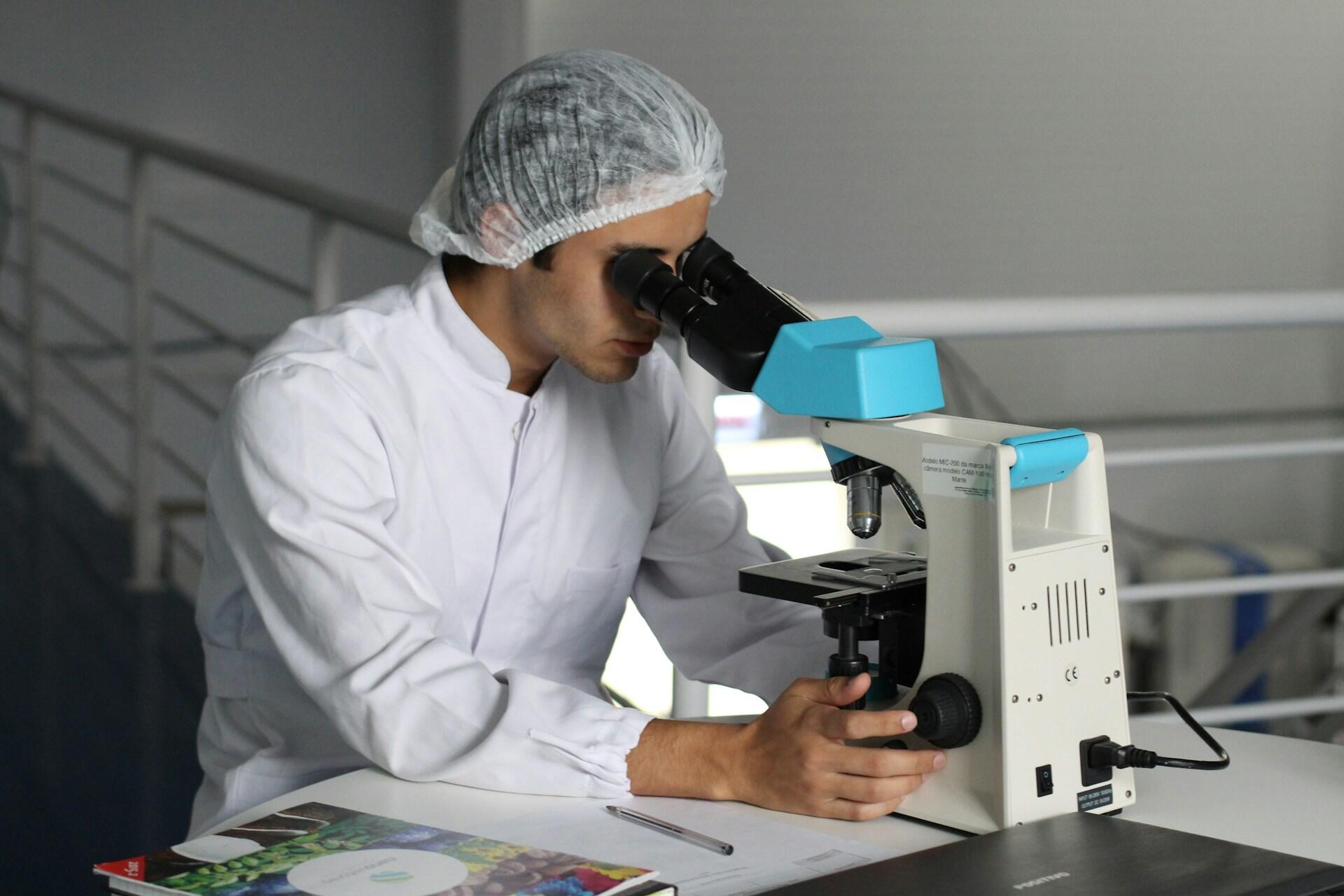 Hombre con delantal blanco y cofia mirando por el microscopio.