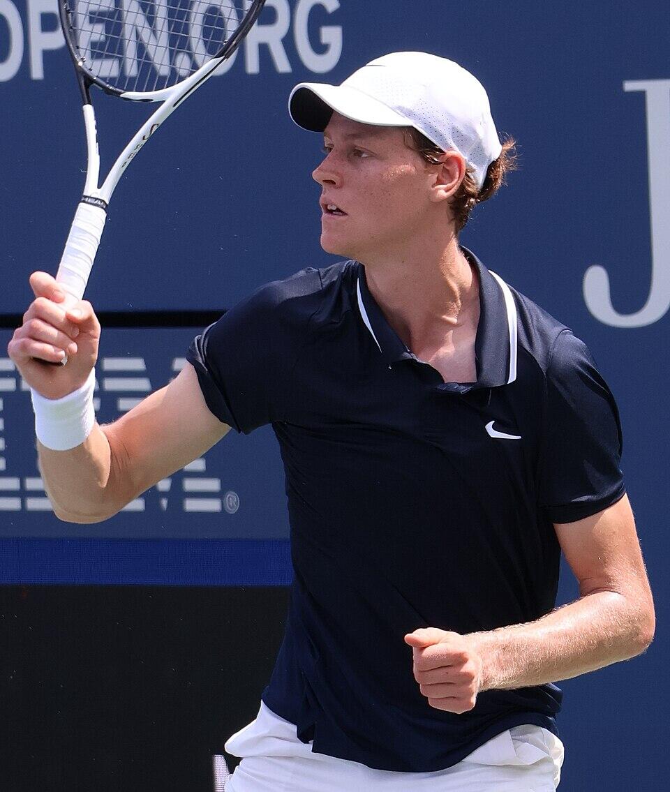 Joven con remera azul y gorra blanca sosteniendo una raqueta de tennis.