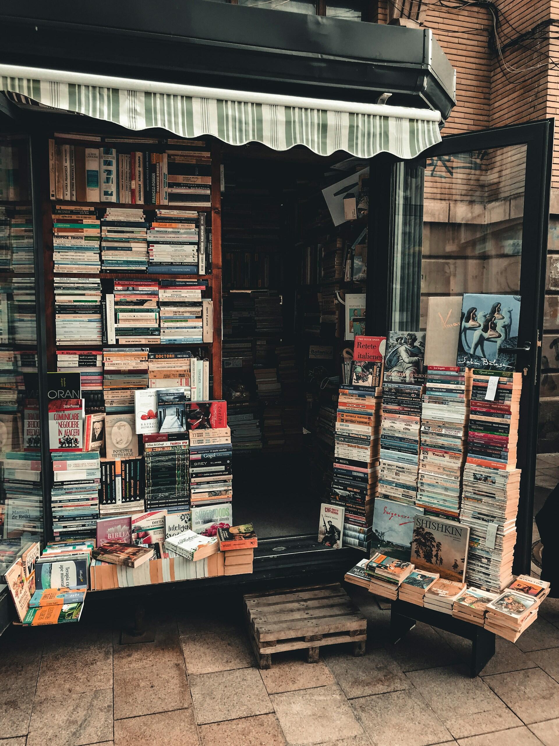 Puerta de pequeña librería independiente con libros apilados en la entrada. Fotografía callejera. Fuente: Unsplash