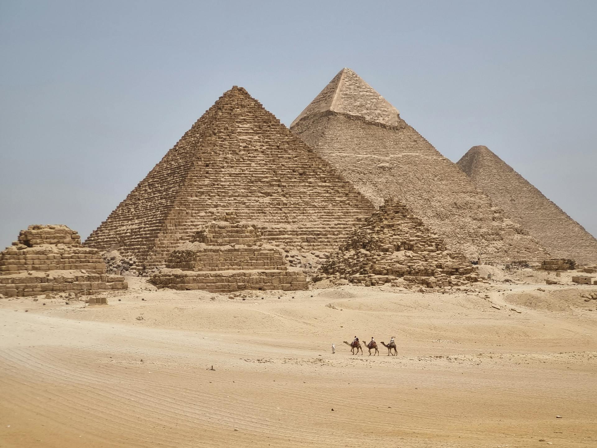 Vista panorámica de las pirámides de Giza con jinetes de camellos en primer plano bajo un cielo despejado.