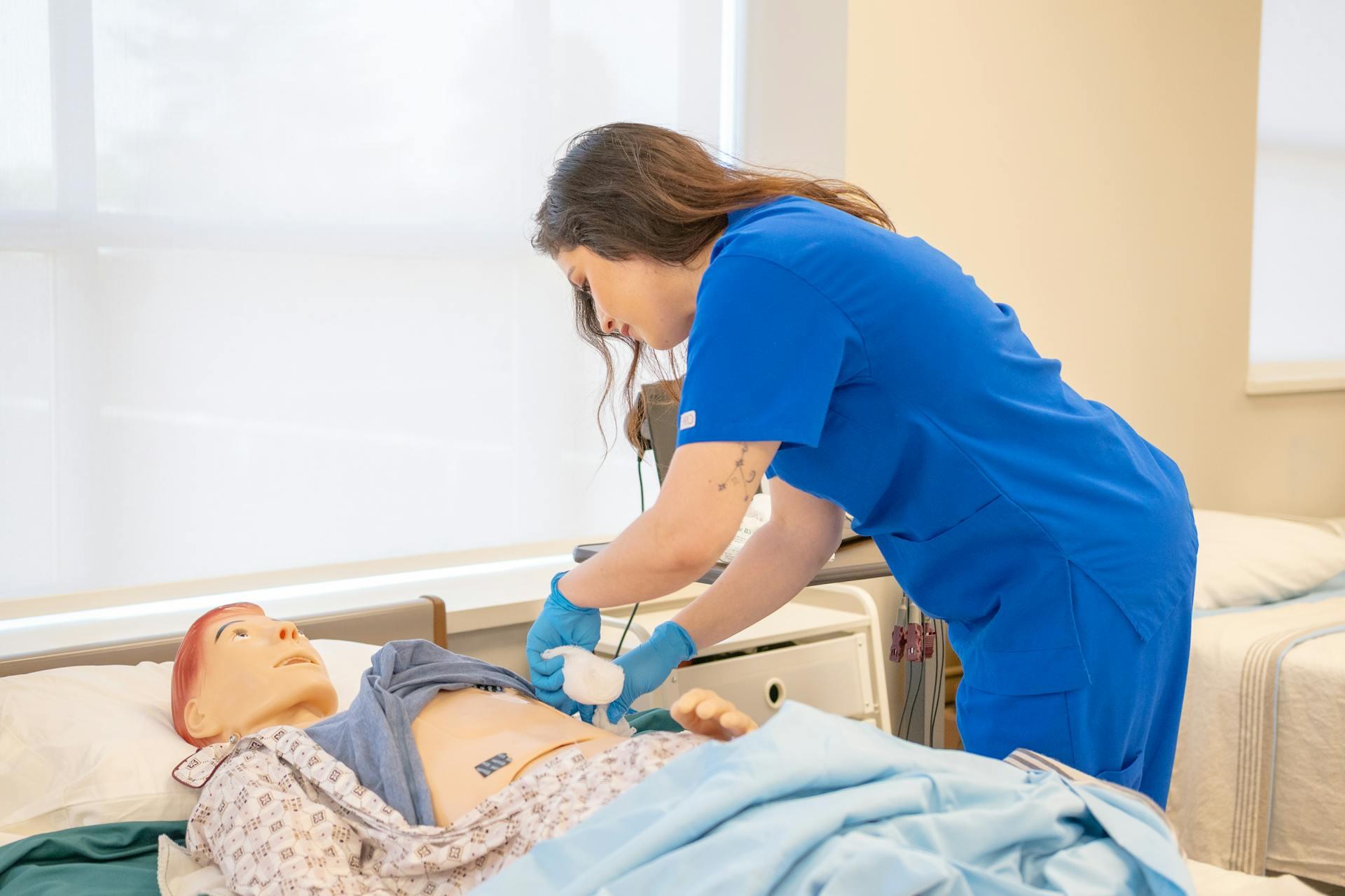 Mujer con uniforme azul practicando procedimientos médicos en un maniquí de entrenamiento de hospital.