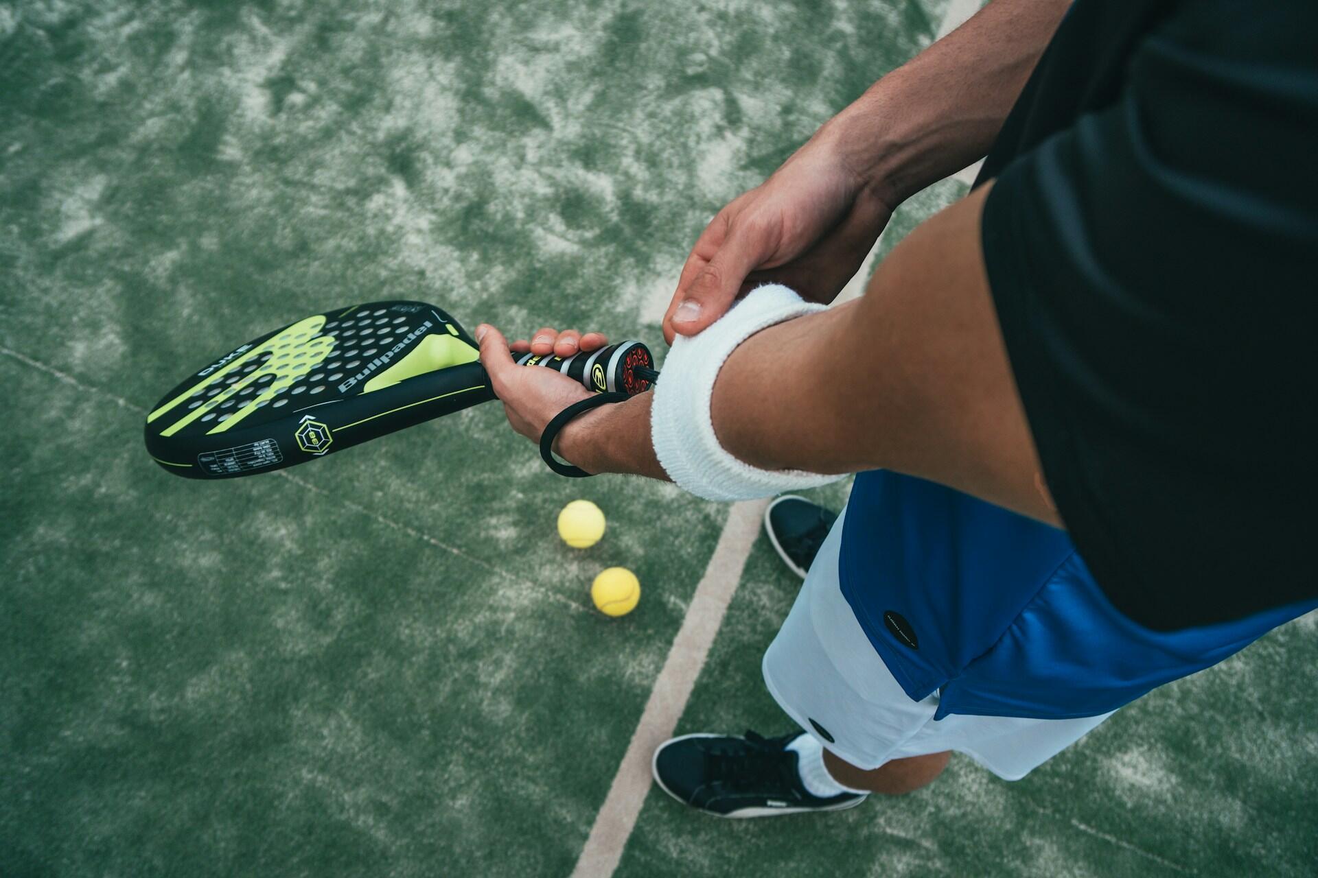 Jugador de pádel preparándose con su paleta y muñequera sobre una pista de césped sintético. Fuente: Unsplash.