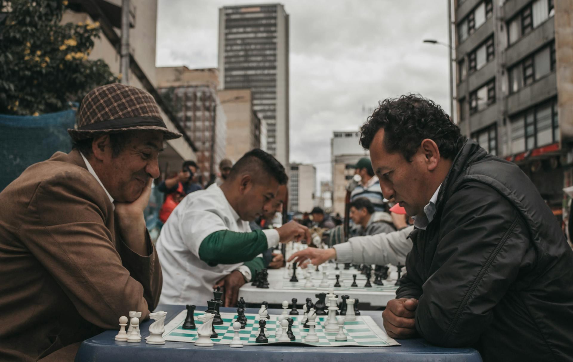 Personas jugando ajedrez sobre mesas entre los edificios.