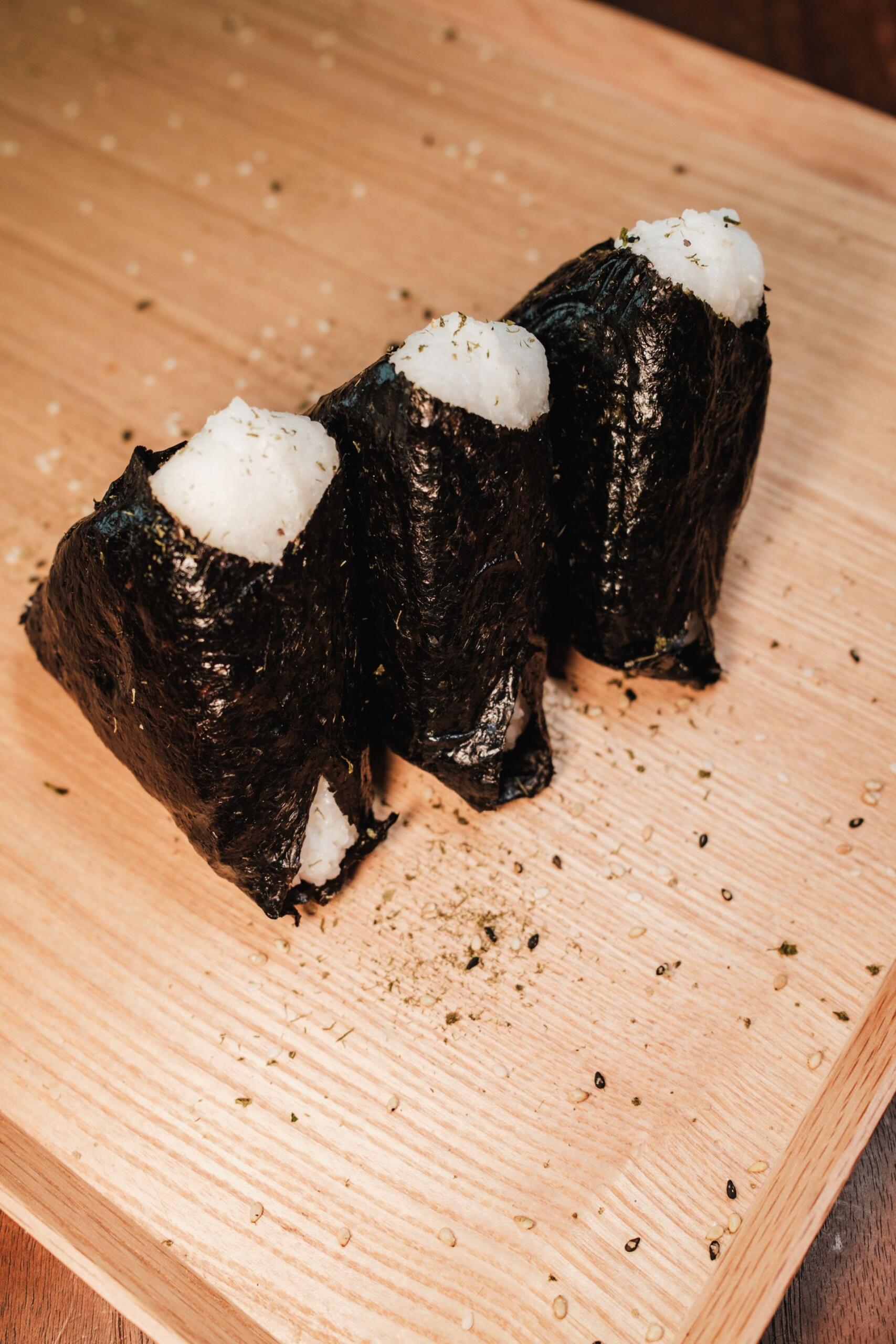 Bolas de arroz envueltas en alga sobre una tabla de madera.