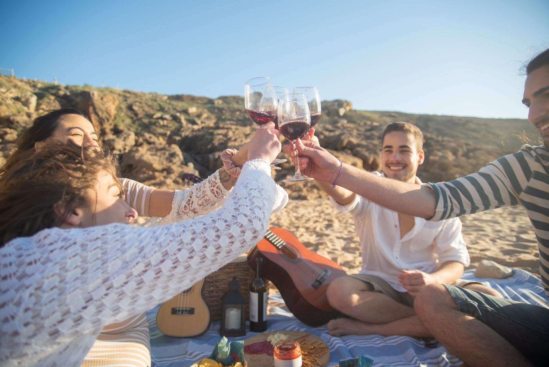 Gente en la playa brindando con copas de vino.