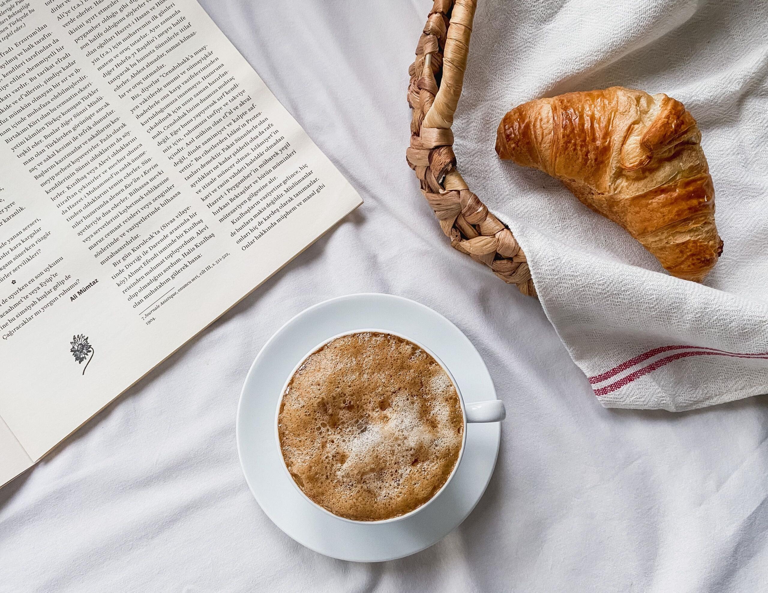 Café y croissant sobre mantel blanco.