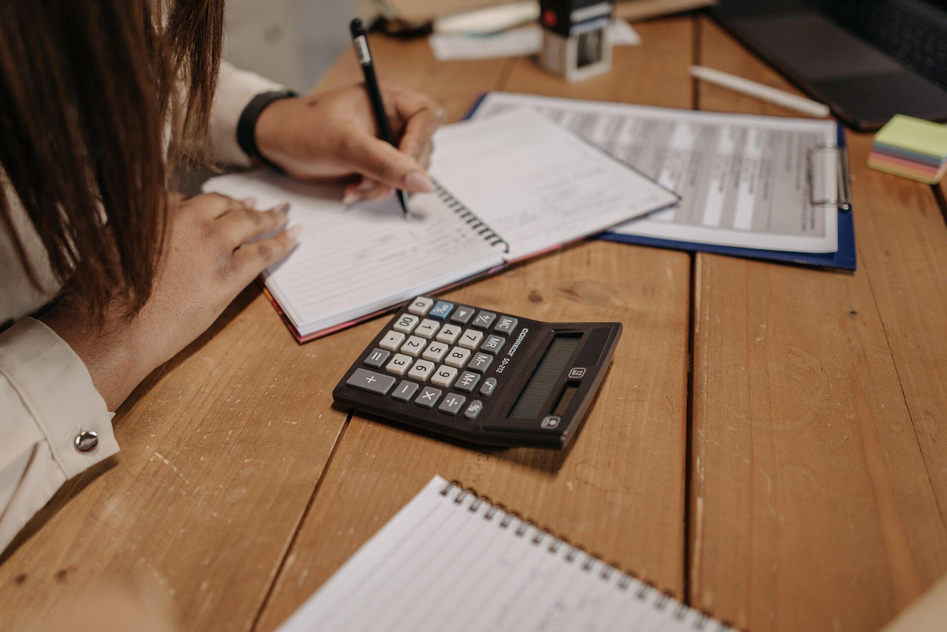 Persona escibiendo sobre el escritorio con calculadora.