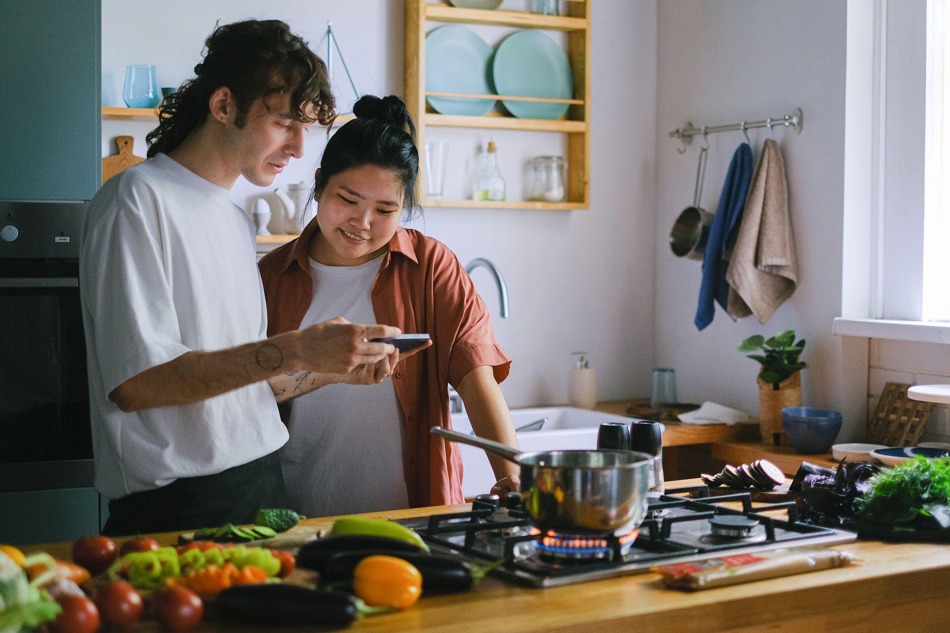 Pareja concinando en la cocina con vegetales sobre la mesa.