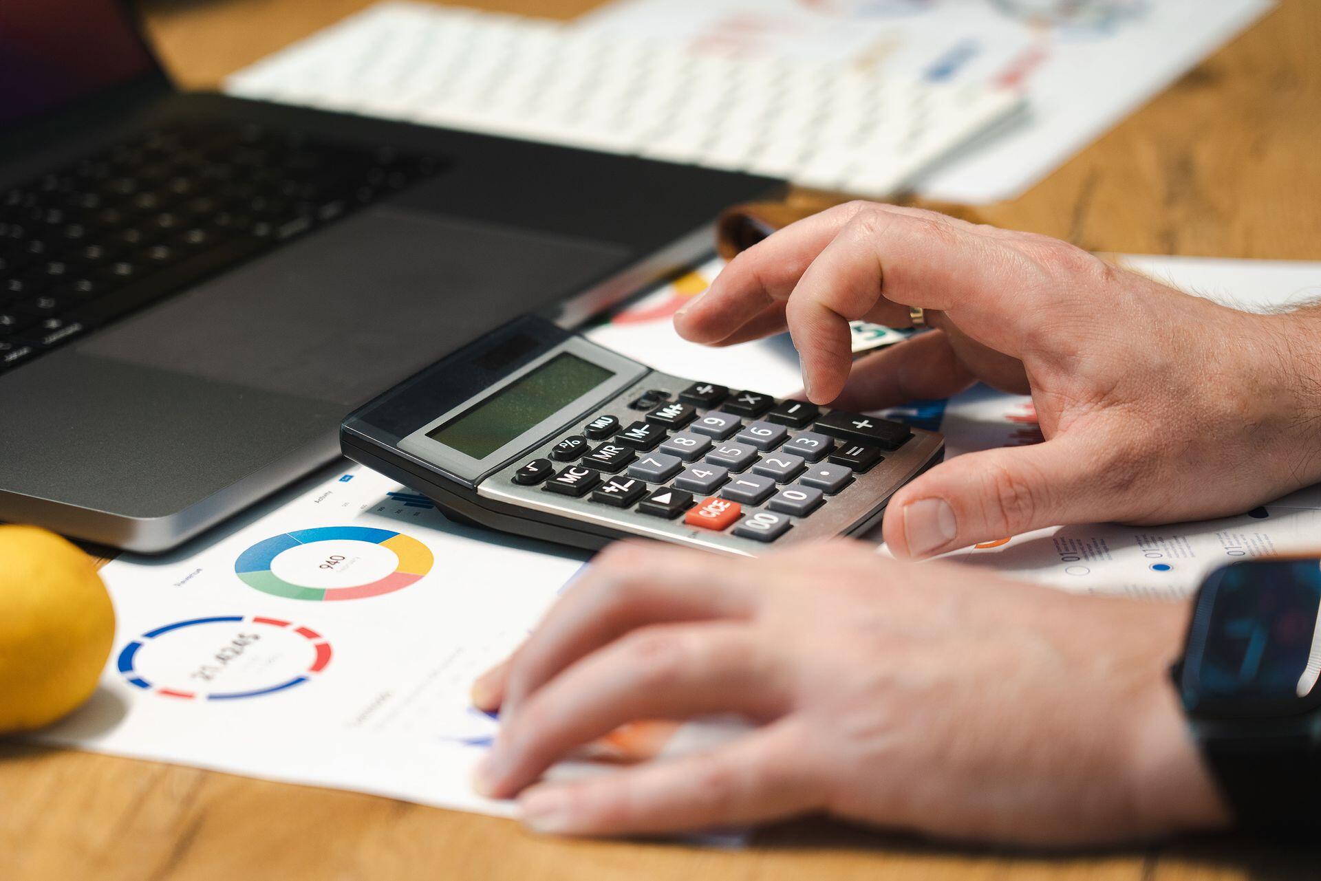 Manos de persona con calculadora y gráficos contables.