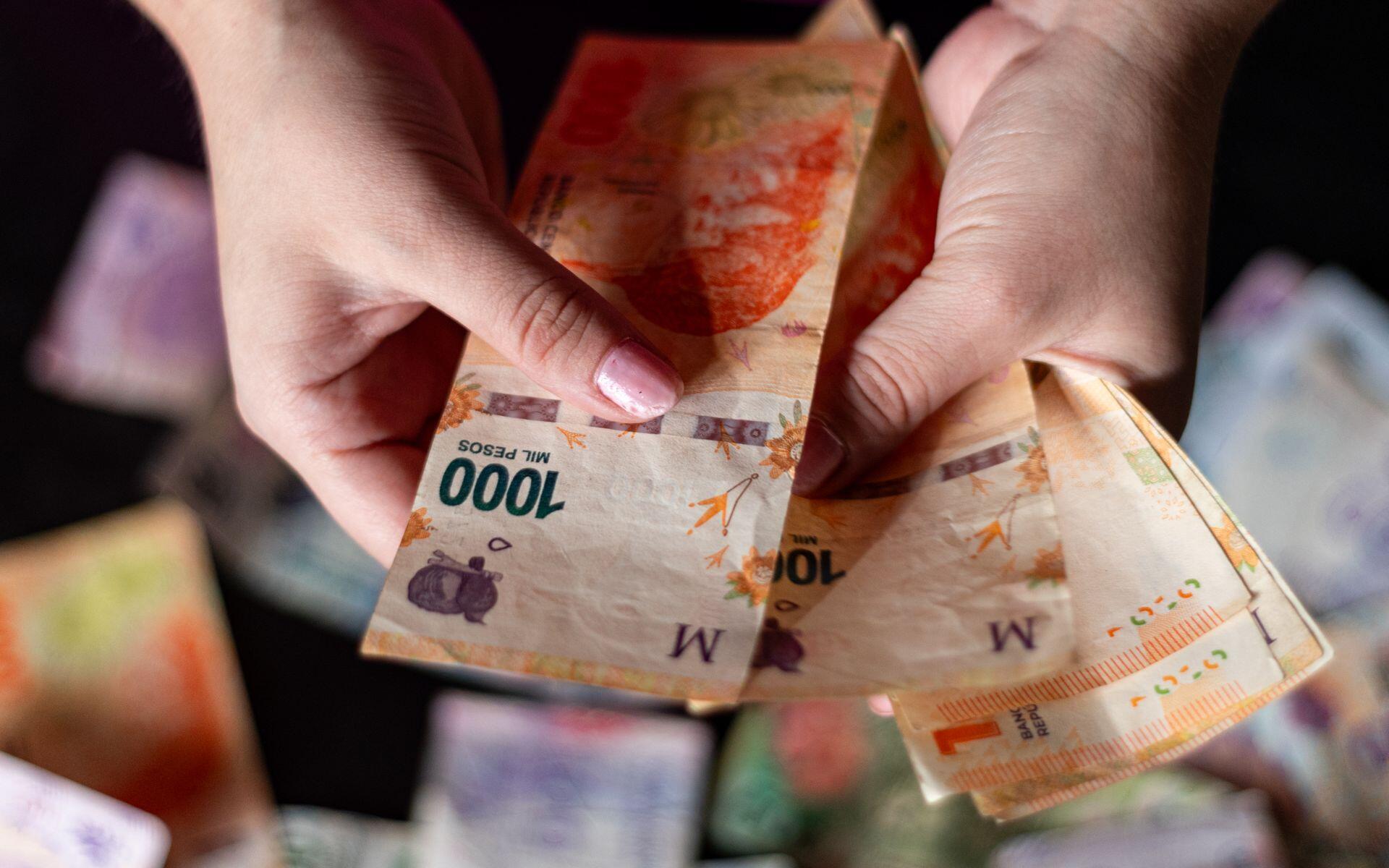 Manos sosteniendo billetes de mil pesos argentinos.