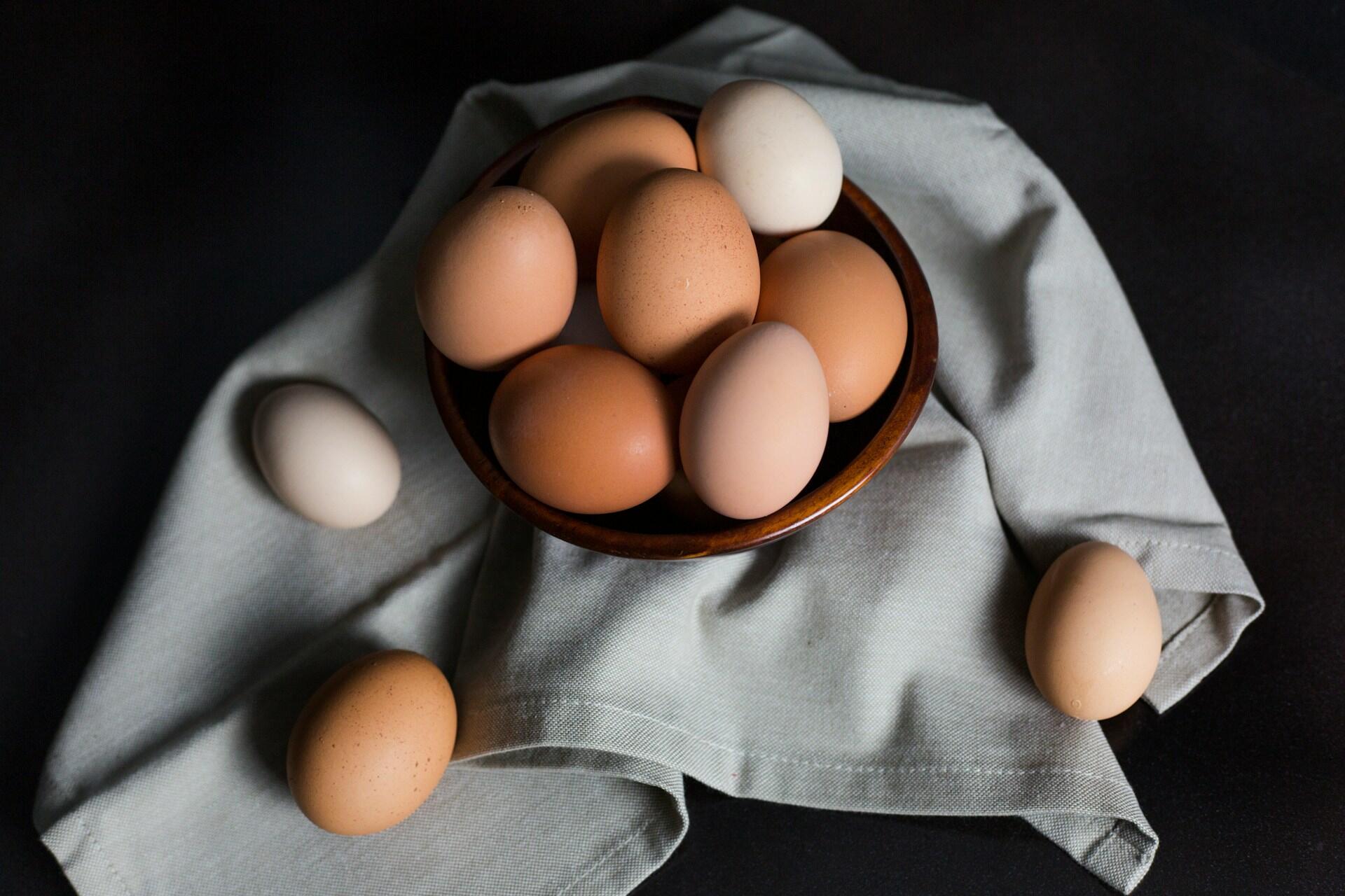 Huevos blancos y marrones sobre un cuenco de madera arriba del repasador blanco.