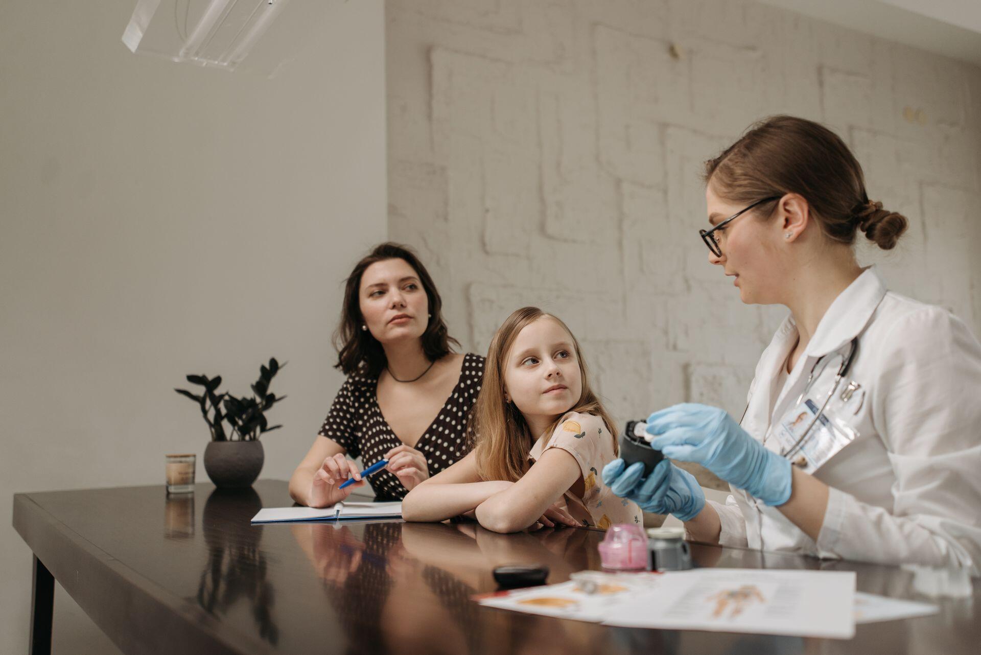 Consultorio médico, una doctora explica un tratamiento a una madre y su hija, por Pavel Danilyuk.