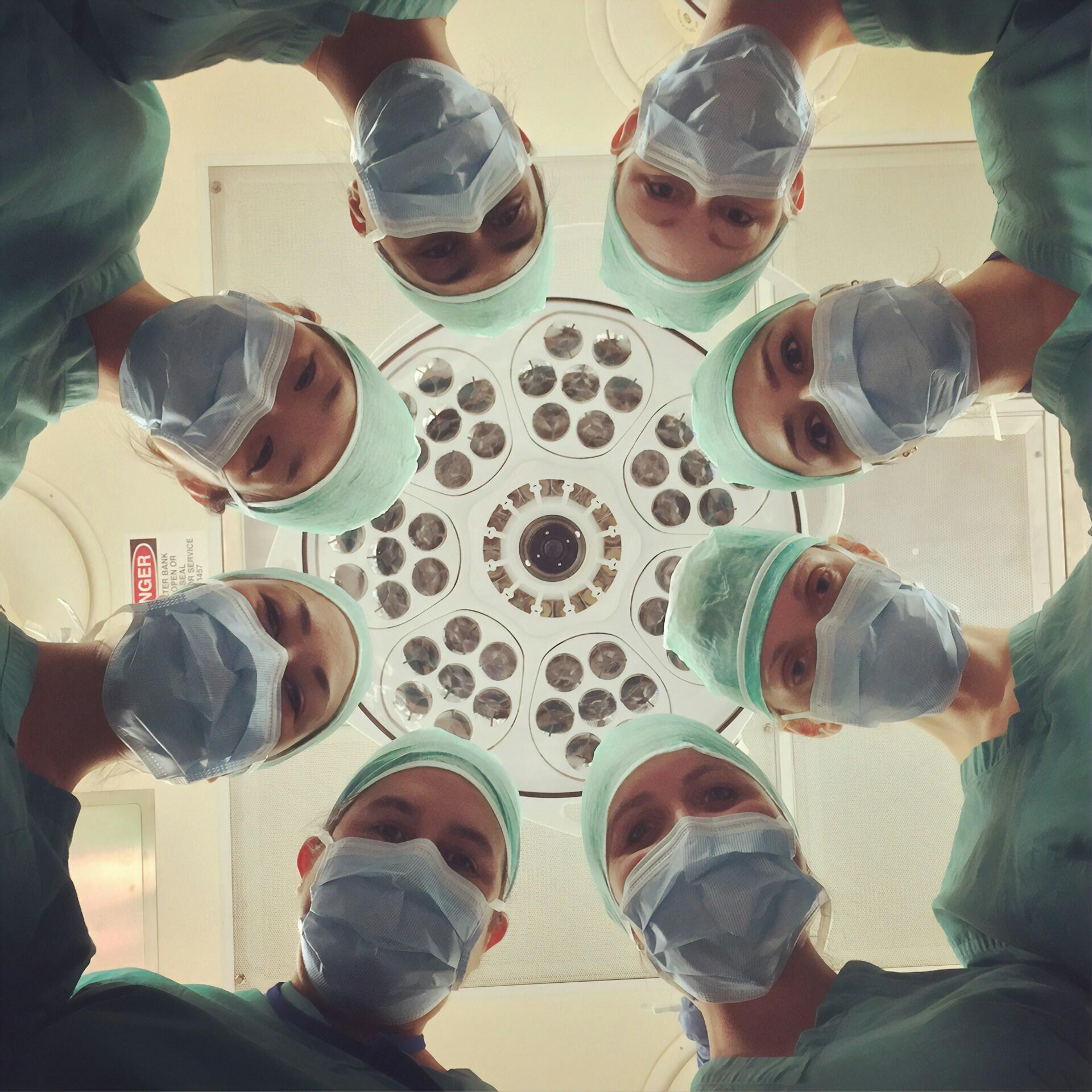 Interior de quirófano, equipo de residentes y médicos mirando hacia abajo bajo la lámpara cialítica. Fuente: Pixabay.