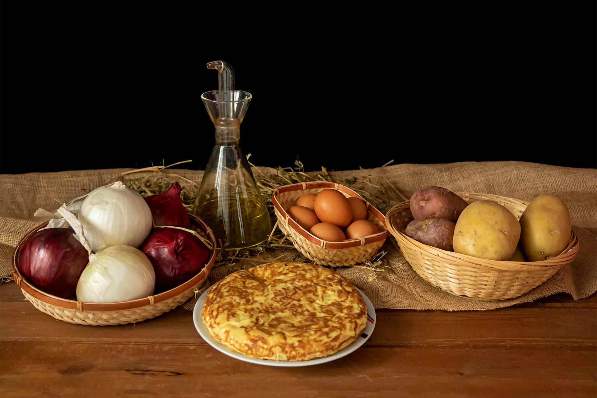 Mesa de madera con canastas de comida y un plato de tortilla de papas.