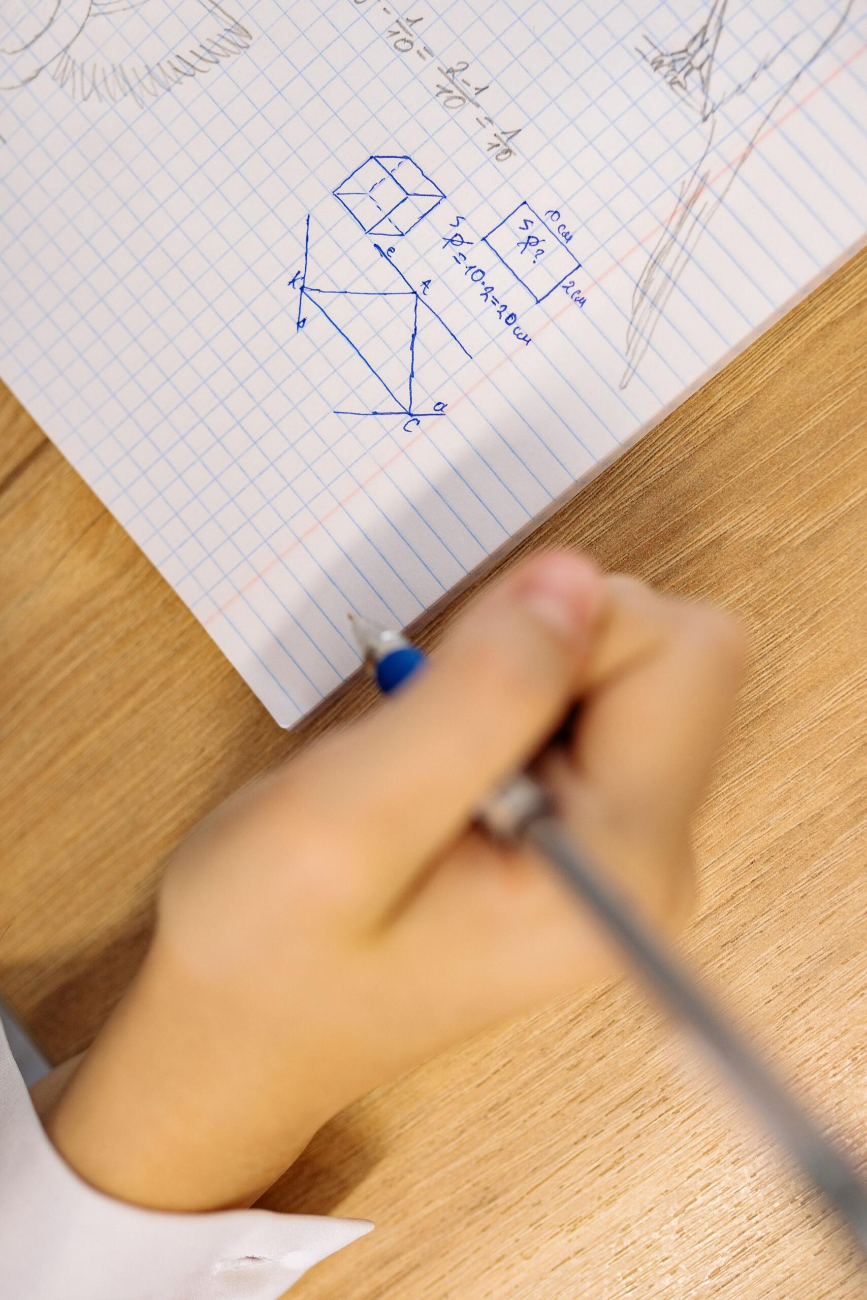 Vista superior de un estudiante anotando fórmulas de área y perímetro en su cuaderno de clase. Fuente: Pexels.