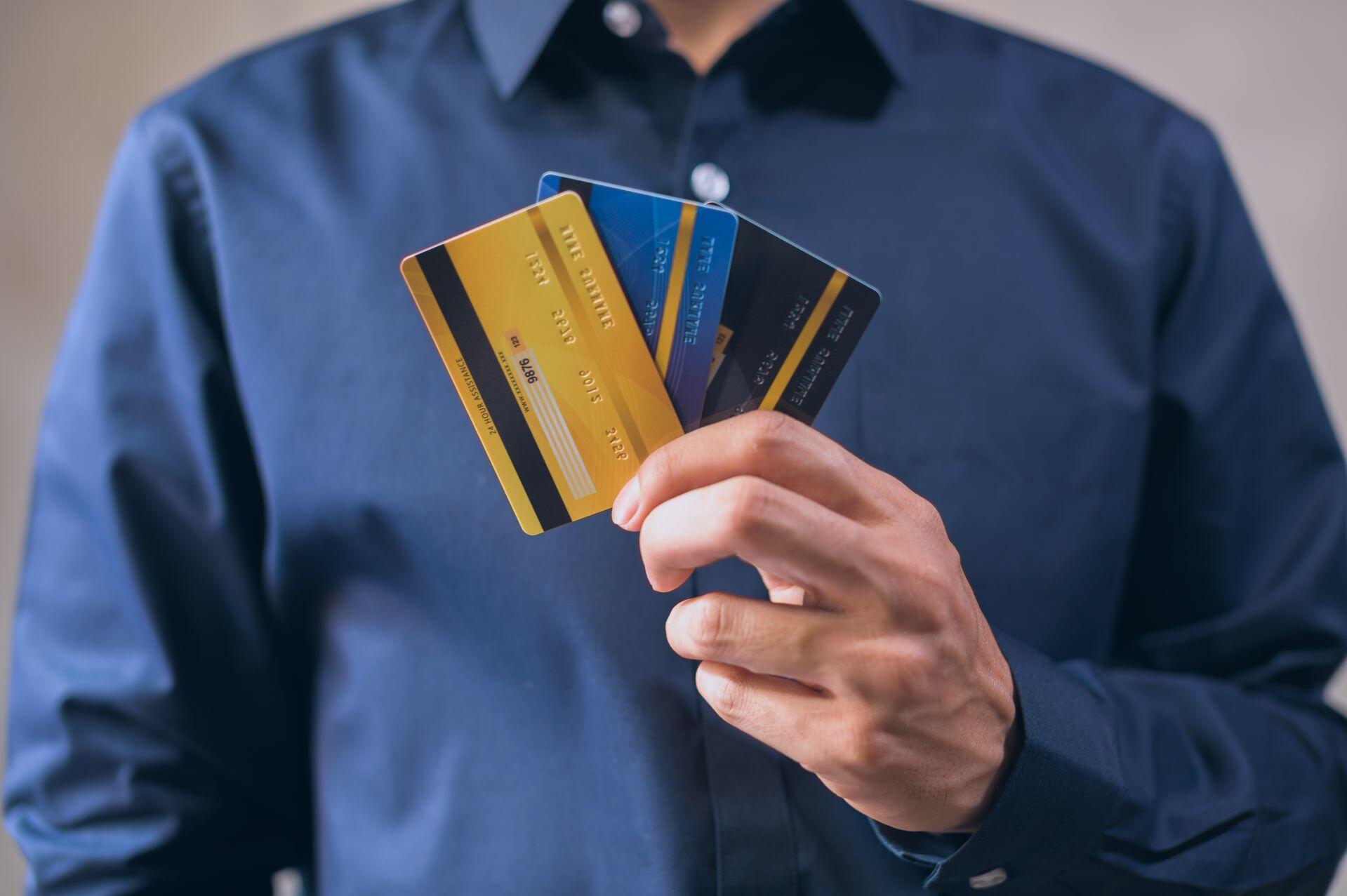 Hombre con camisa azul sosteniendo tarjetas de crédito.
