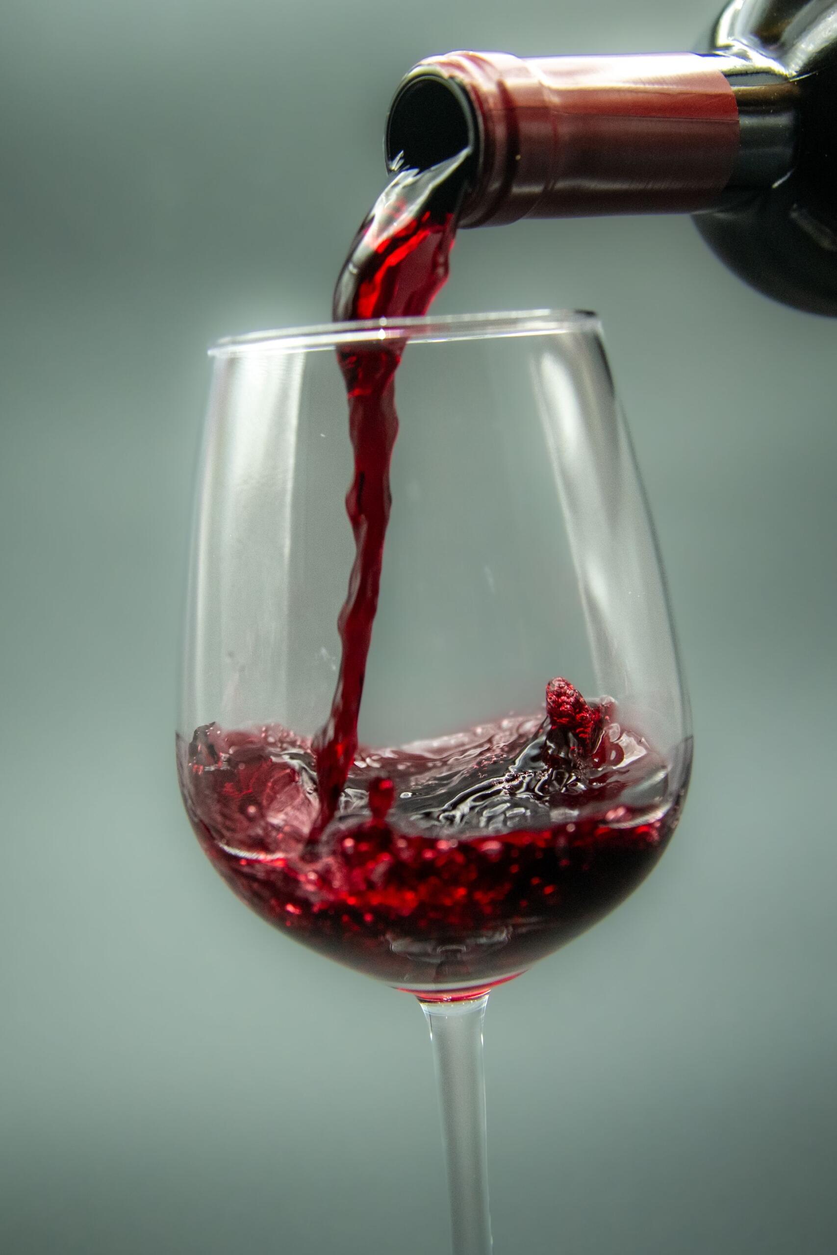 Botella de vino tinto sirviendosé sobre una copa de vidrio.