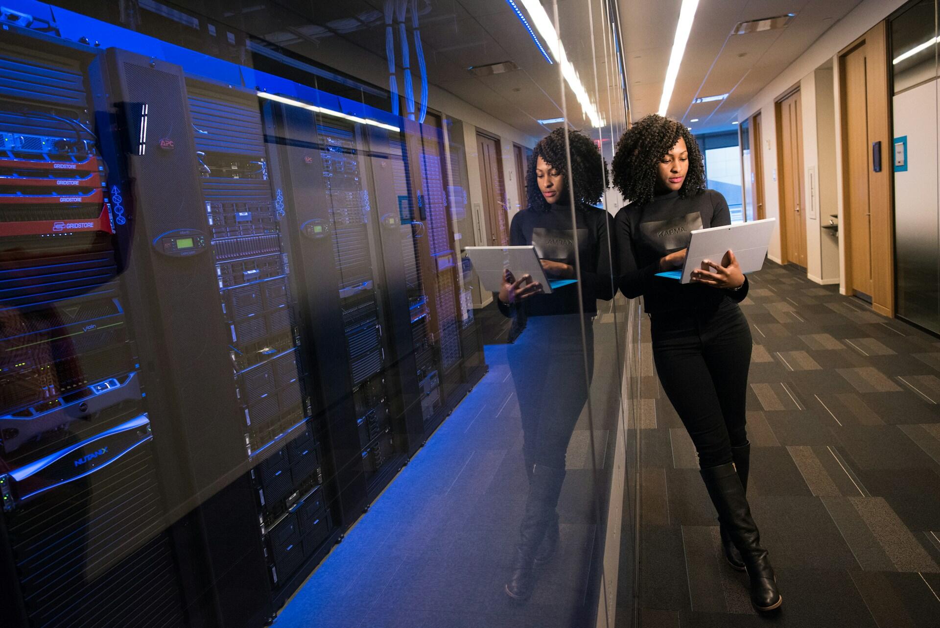 Una profesional con la computadora frente a racks de servidores en un centro de datos. Fuente: Christina @ wocintechchat.com.