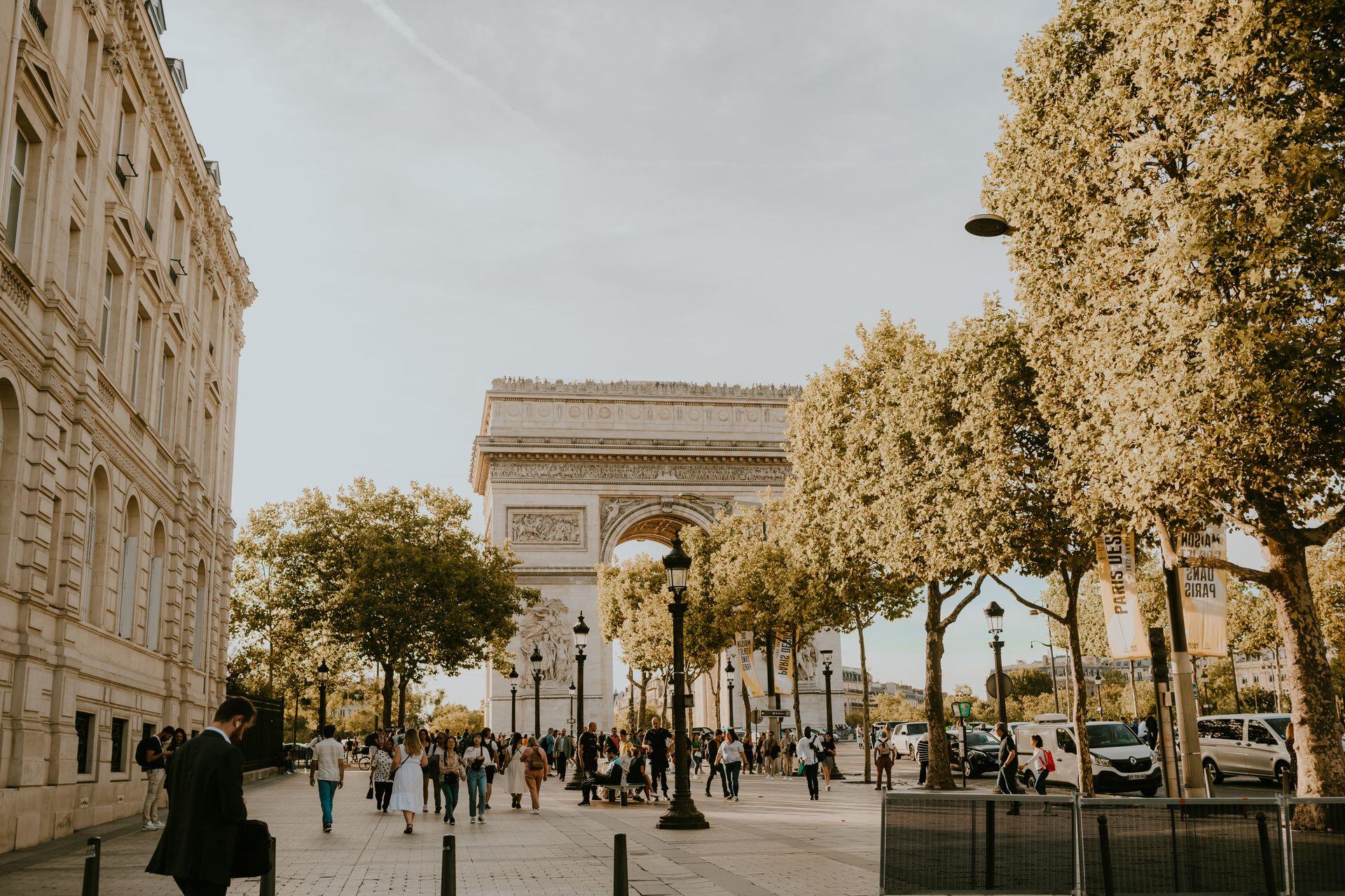 Vista del icónico Arco de París con gente caminando sobre la calle arbolada.