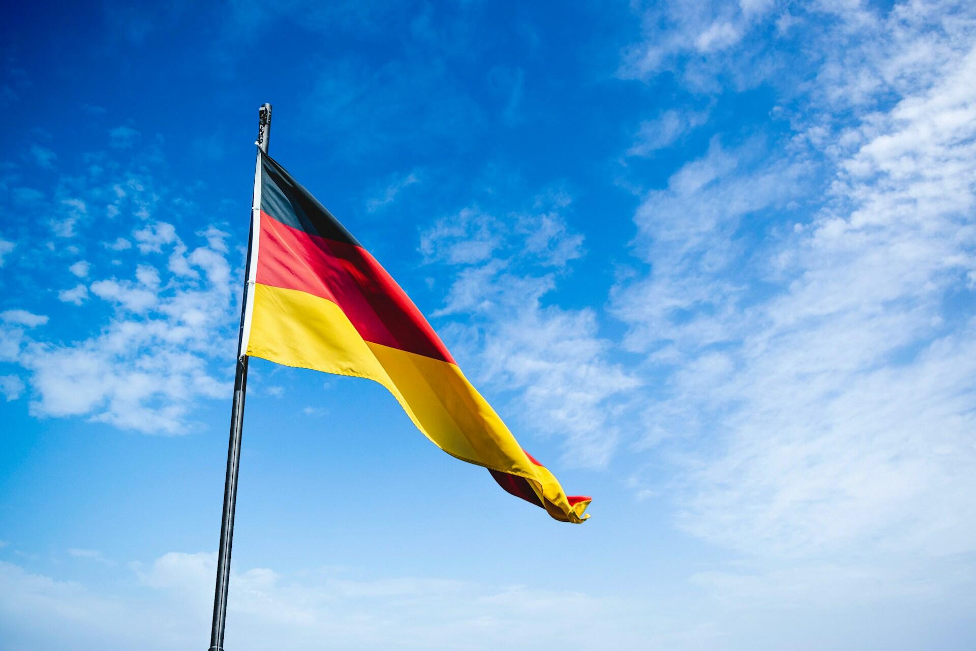 Alemania, bandera alemana flameando bajo un cielo azul, Christian Wiediger / Unsplash.