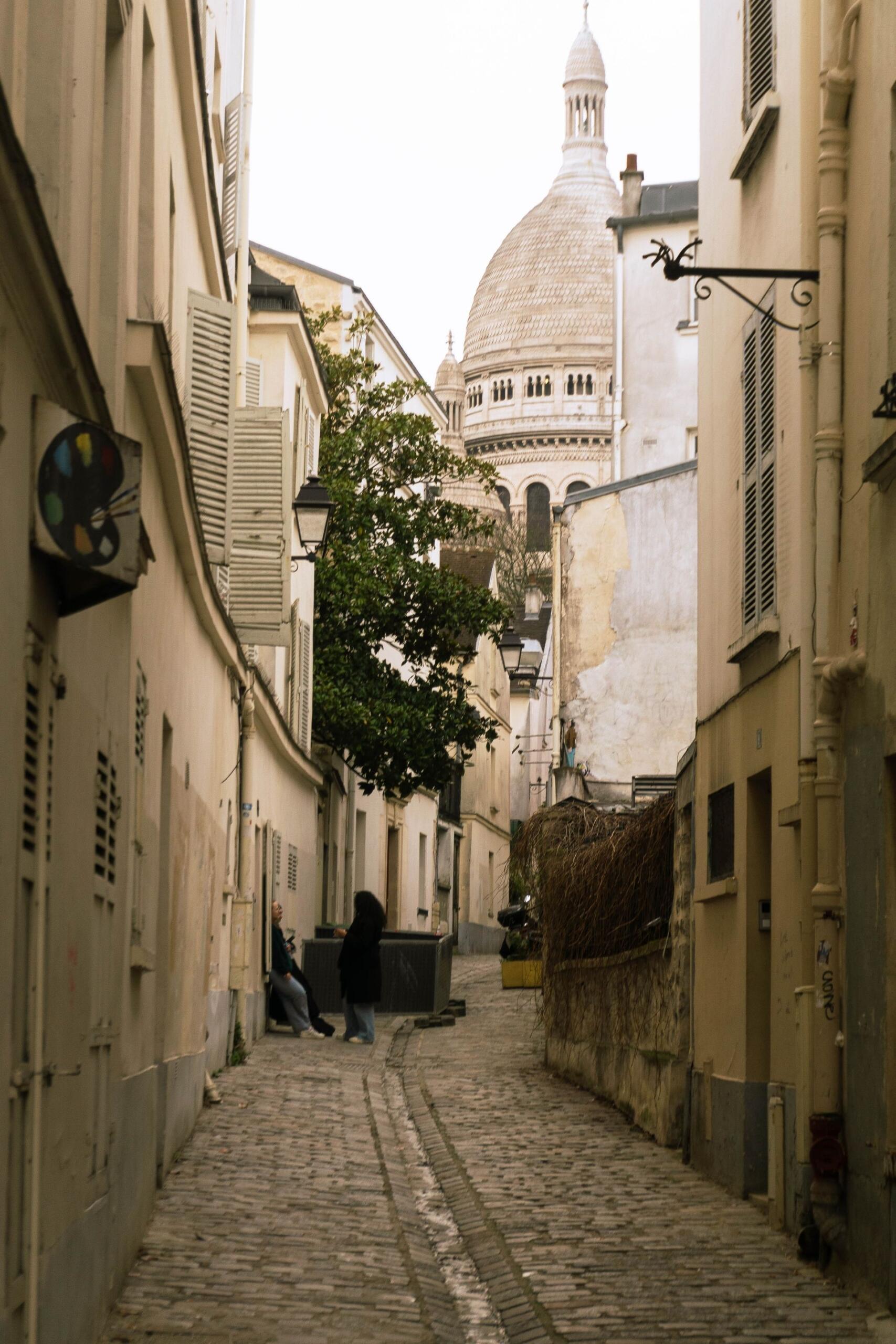Pintoresca calle adoquinada en Montmartre, París, con vistas a la icónica basílica del Sacré-Cœur.
