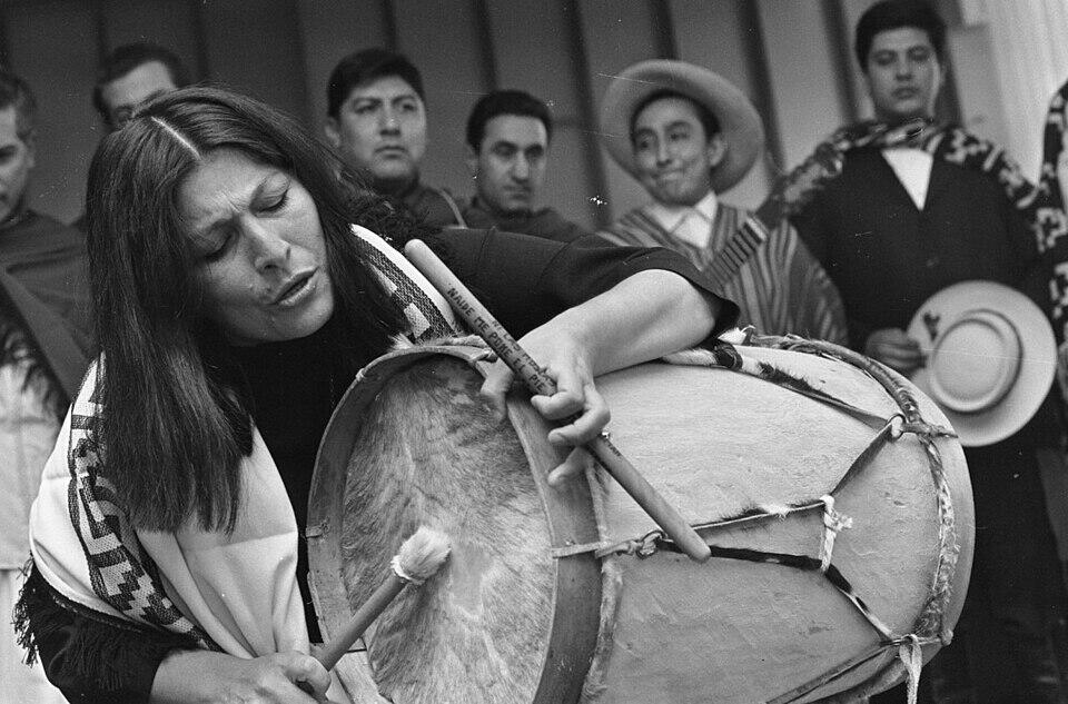 Mercedes Sosa tocando el bombo delante de hombres con pocho y sombrero.
