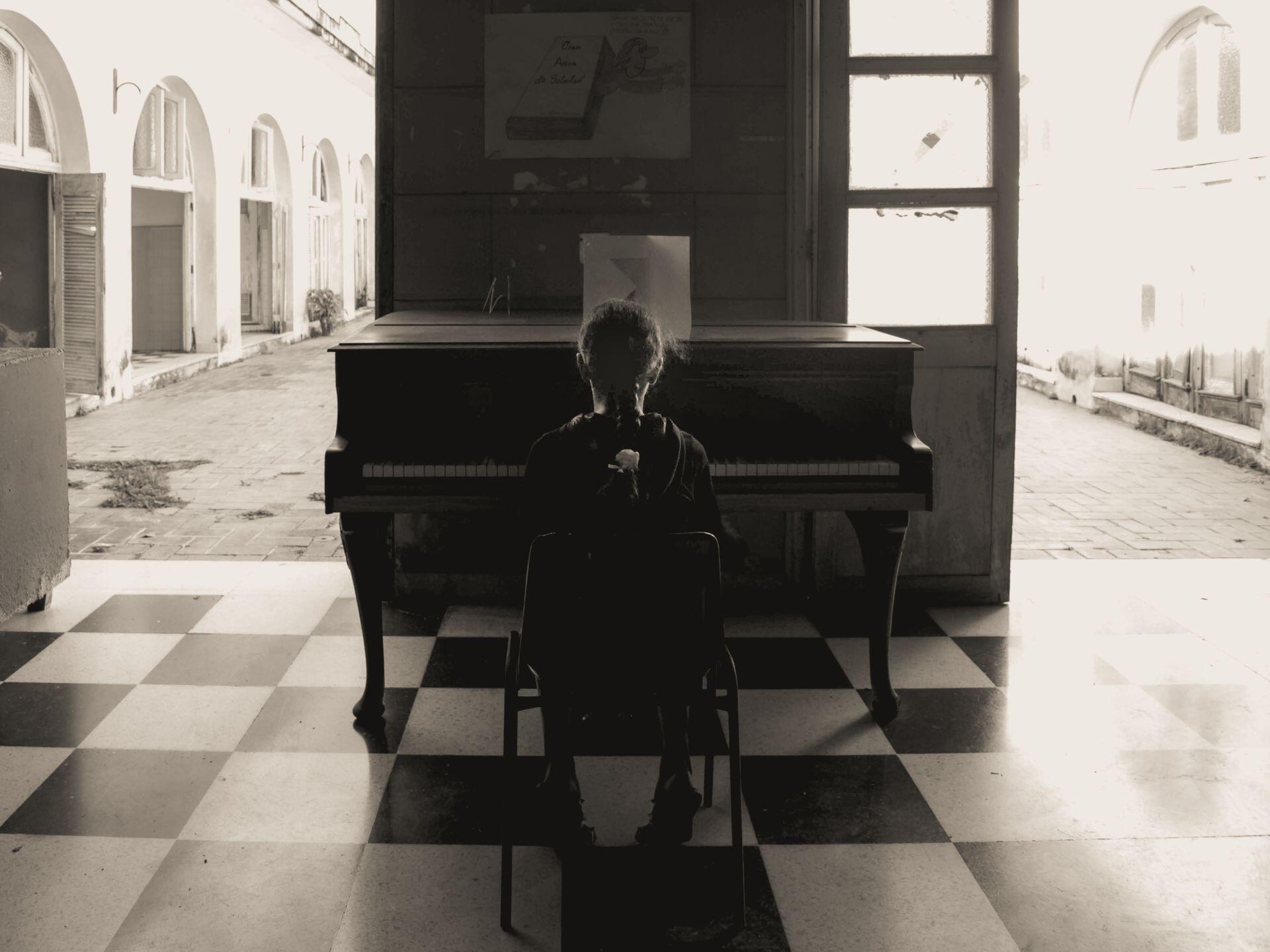 Niña sentada frente al piano al lado de las ventanas.