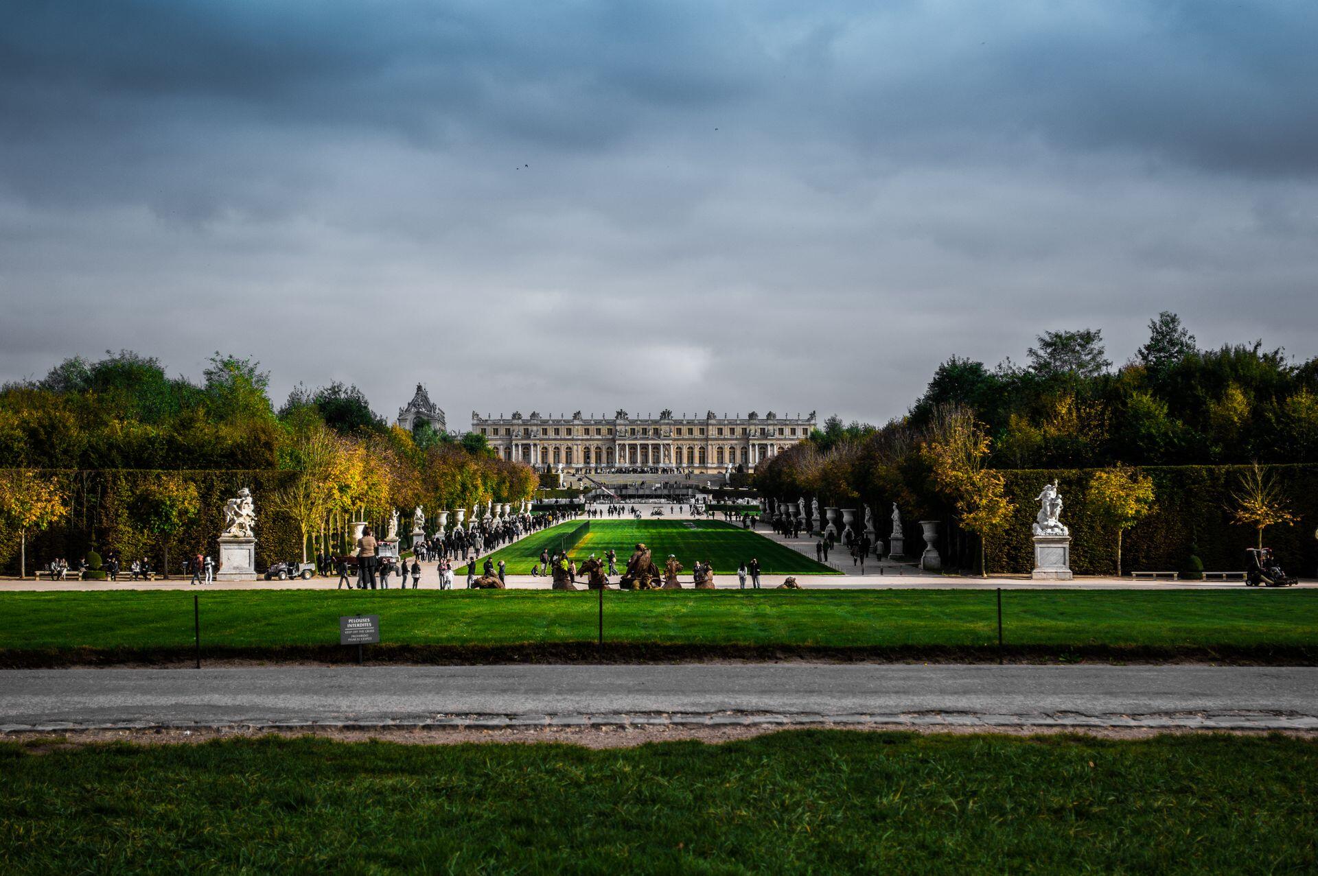 Palacio de Versalles rodeado de jardines con árboles y esculturas.
