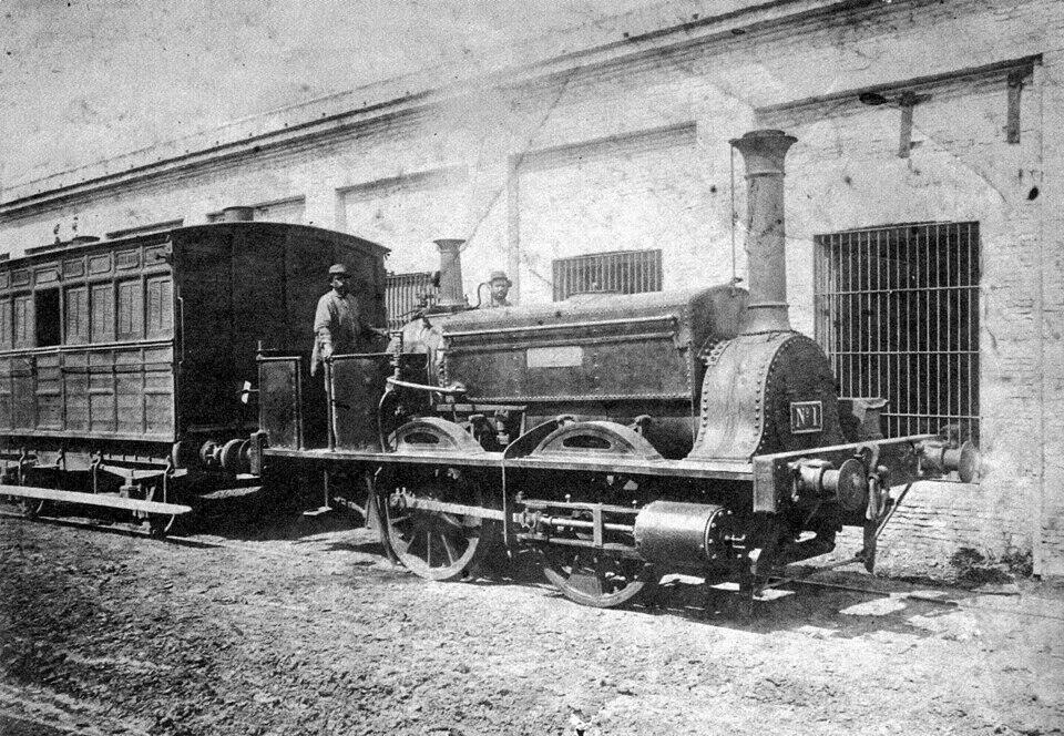 Locomotora antigua con chofer delante de la estación.