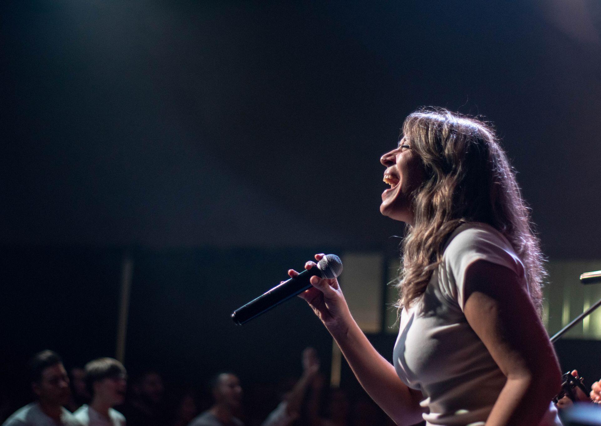 Escenario de concierto nocturno con una mujer cantando con pasión y técnica vocal de perfil, por Franco Monsalvo.