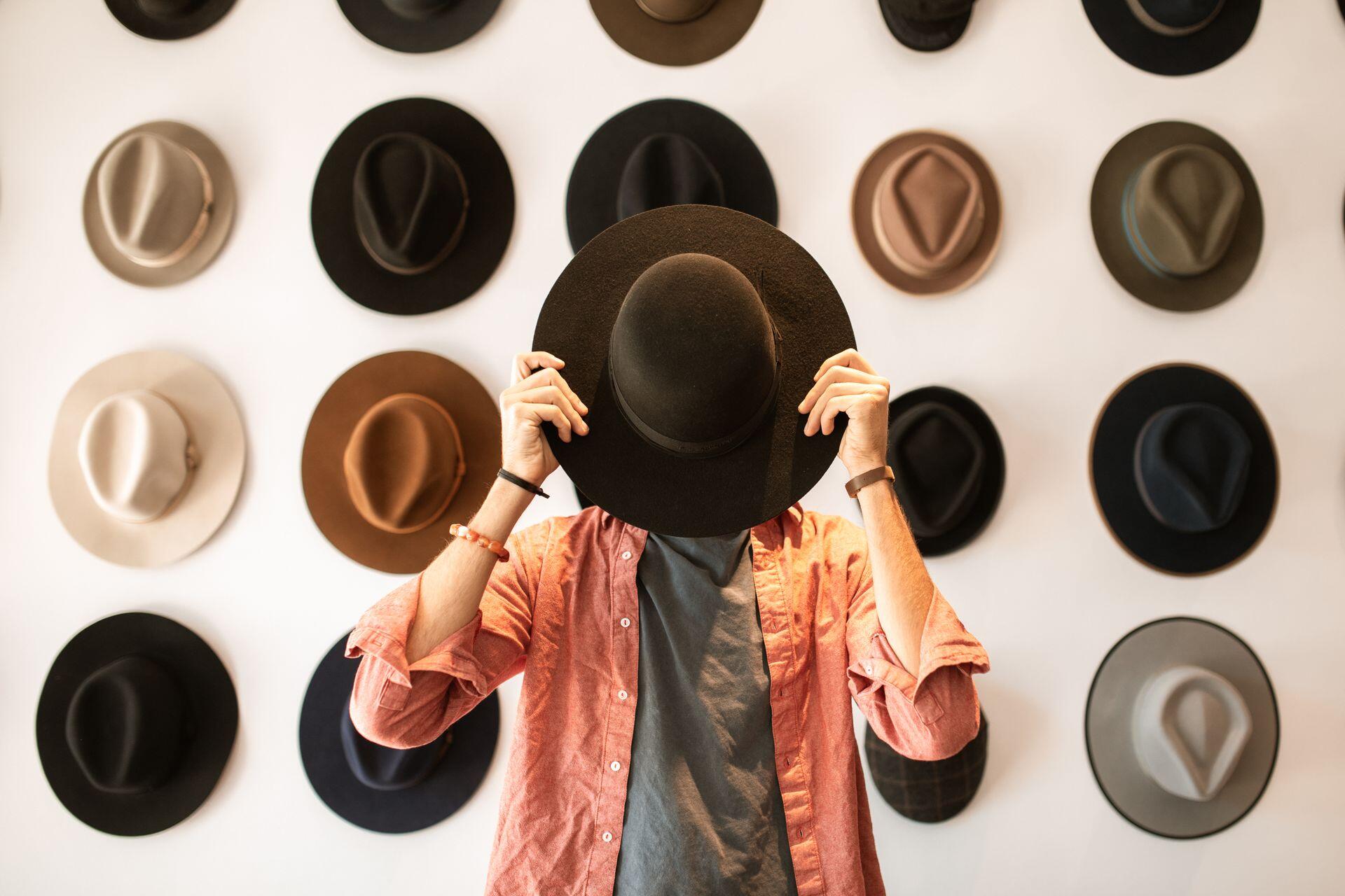 Hombre parado delamte de los sombreros con la cara tapada.