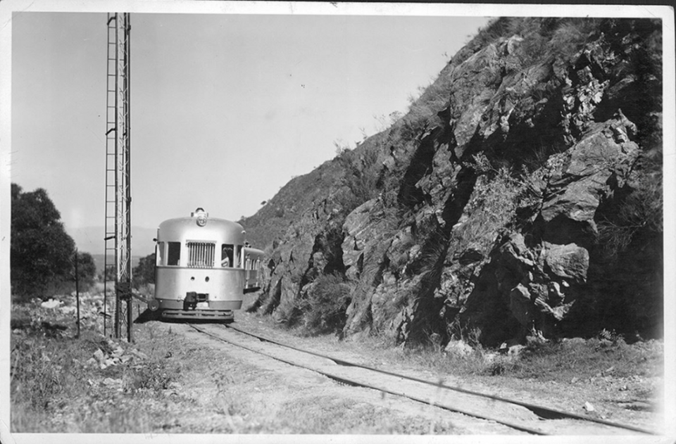 Foto en blanco y negro de un tren en las vías al lado de las rocas.