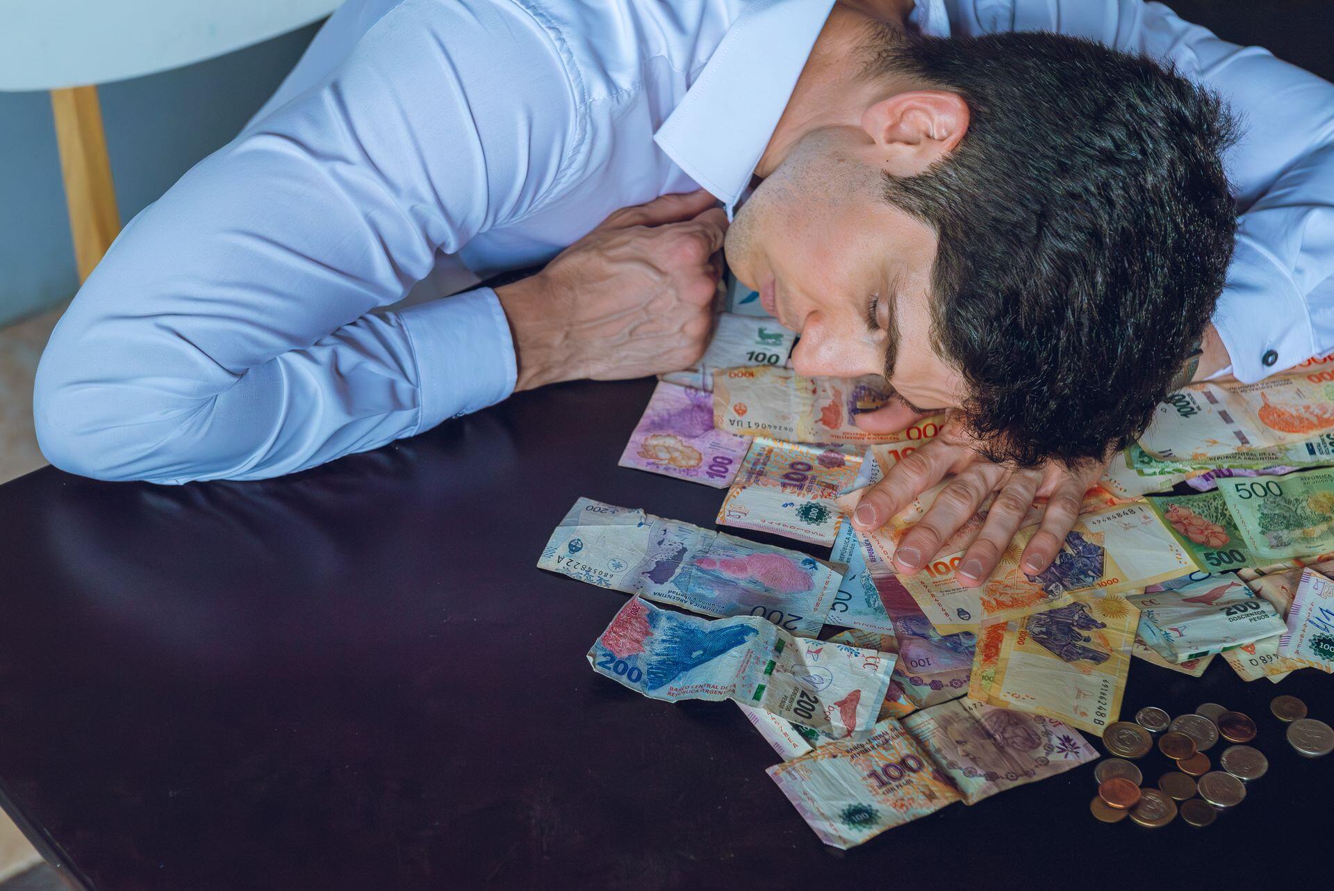 Hombre con la cabeza apoyada sobre la mesa con dinero.