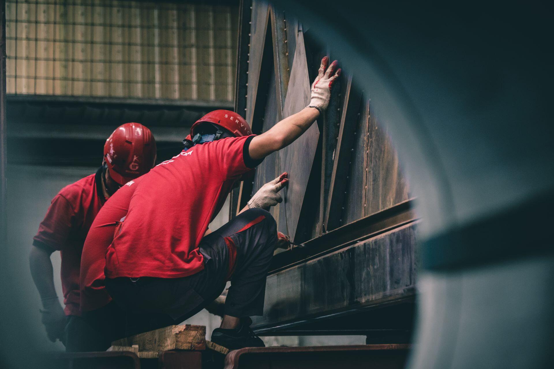 Hombres trabajando en la fábrica con remeras y casos rojos.