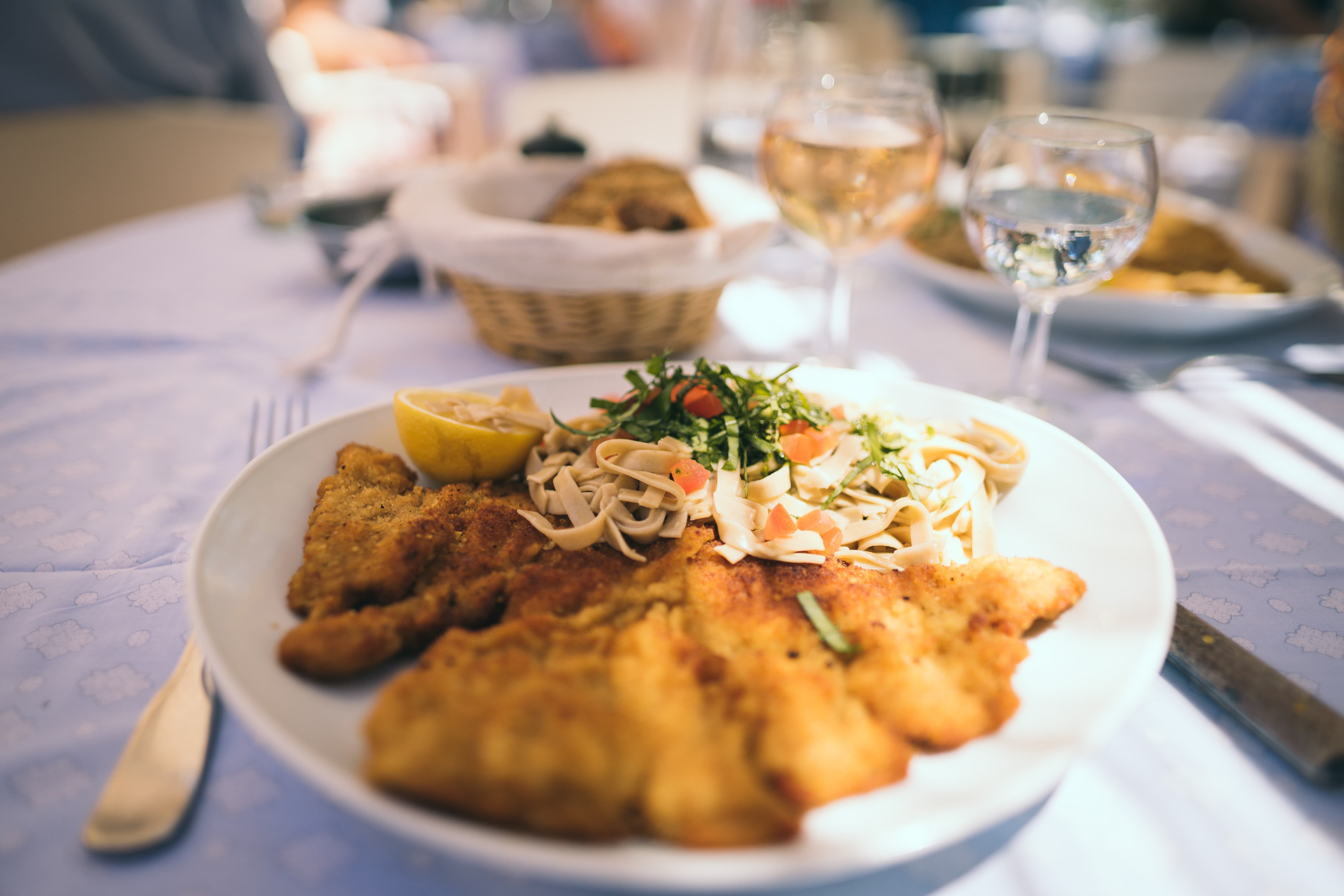 Wiener Schnitzel mit Ruccola, Brot und zwei Gläser Wein auf einem Restauranttisch