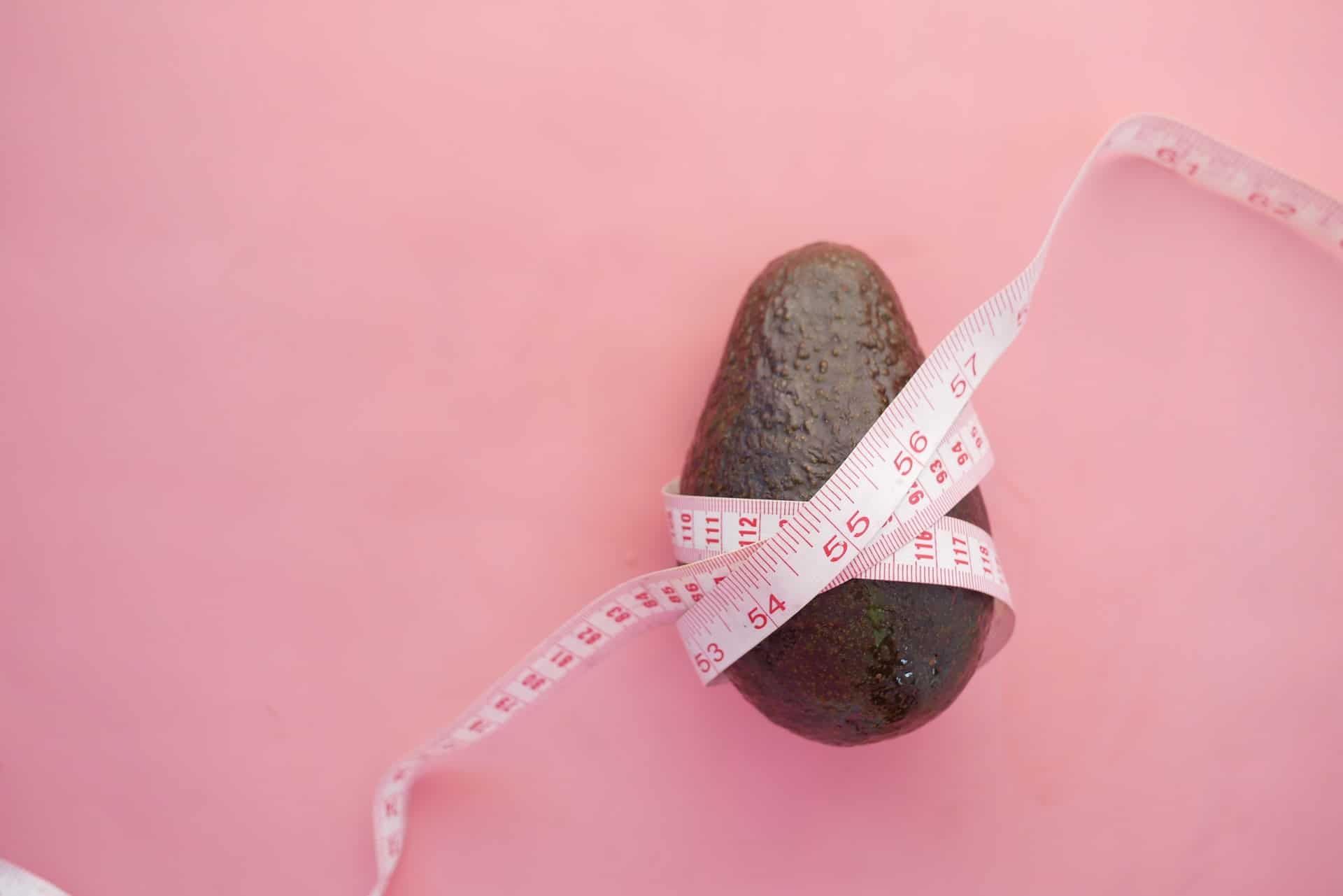 Avocado mit Maßband umwickelt liegt auf rosa Untergrund