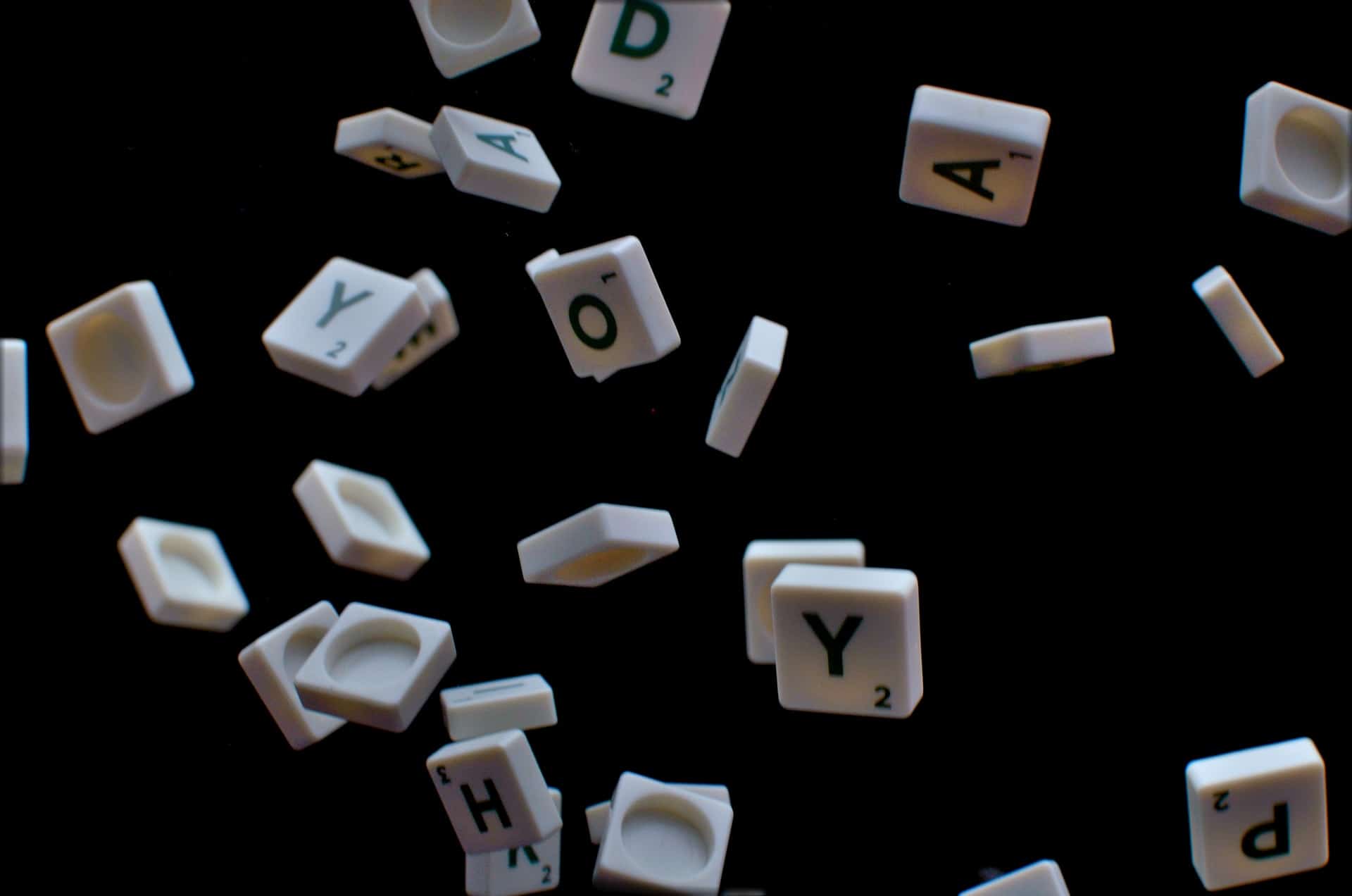 Buchstaben des Spiels Scrabble schweben in der Luft vor einem schwarzen Hintergrund.