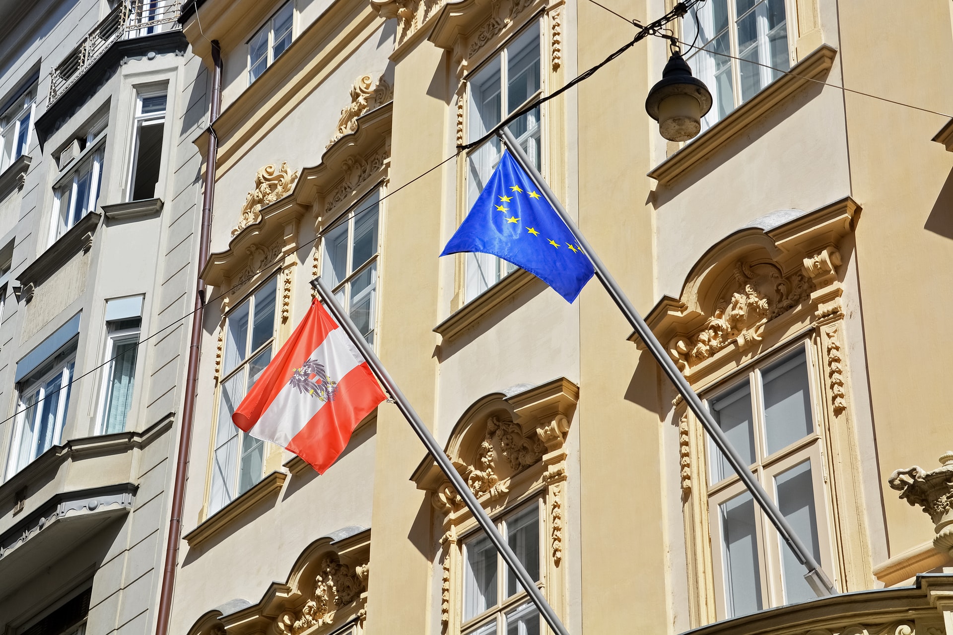 Die österreichische und die europäische Flagge wehen am Wind auf der Seite eines Altbau-Gebäudes.